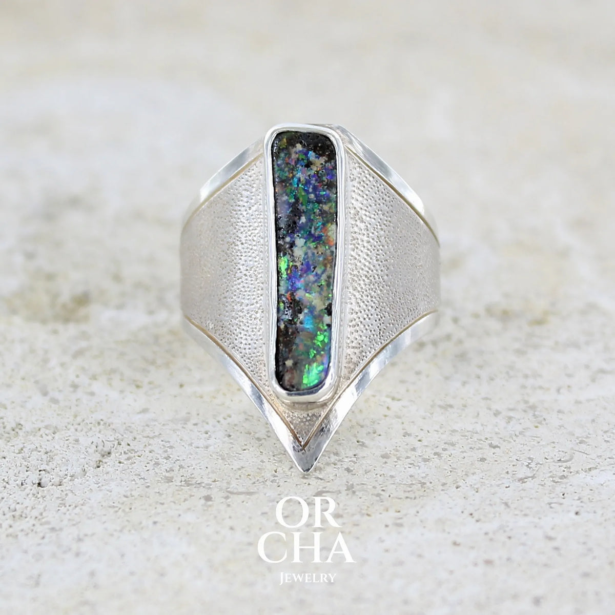 Bague pour femme en argent massif 925 sertie d'une opale boulder aux feux multicolores. Cabochon d'opale massive naturelle taillée en forme de rectangle.. Pierre de qualité opaque. Bague unique réalisée en taille 55 par Orcha Jewelry.