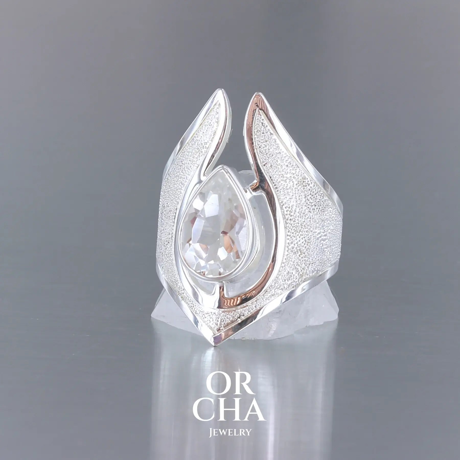 Grande bague pour femme en argent massif sertie d'une Topaze blanche, collection Bastet. Pierre facettée en forme de goutte, pierre naturelle incolore avec un très bel éclat. Pierre fine de qualité transparente propre à l'oeil. Disponible en plusieurs tailles. Bijoux unique, éthique et durable présenté dans un coffret de notre marque, prêt à offrir. Livraison offerte, certificat d'authenticité, service client.