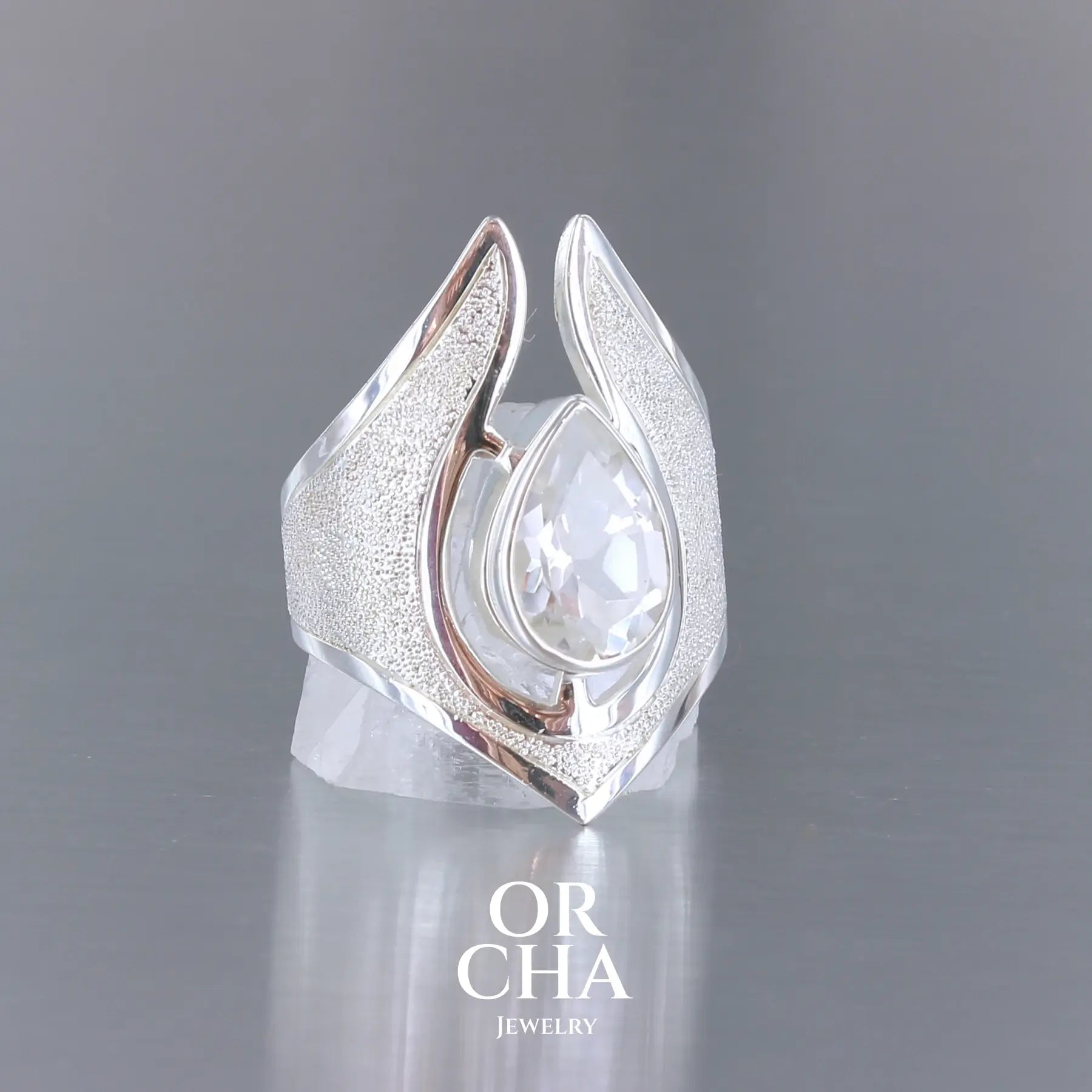 Grande bague pour femme en argent massif sertie d'une Topaze blanche, collection Bastet. Pierre facettée en forme de goutte, pierre naturelle incolore avec un très bel éclat. Pierre fine de qualité transparente propre à l'oeil. Disponible en plusieurs tailles. Bijoux unique, éthique et durable présenté dans un coffret de notre marque, prêt à offrir. Livraison offerte, certificat d'authenticité, service client.