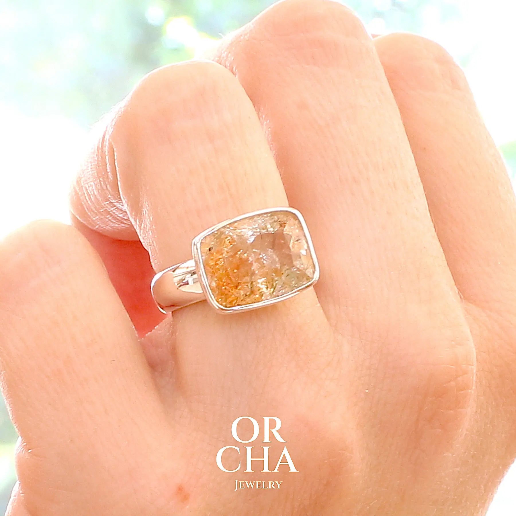 Bague cocktail pour femme en argent massif sertie d'une pierre de soleil oranges de très belle qualité, pierre transparente avec inclusions scintillantes d'hématites.Pierre naturelle facettée de forme rectangulaire. Tailles 54. Bijoux unique, éthique et durable présenté dans un coffret de notre marque, prêt à offrir. Livraison offerte, certificat d'authenticité, service client.
