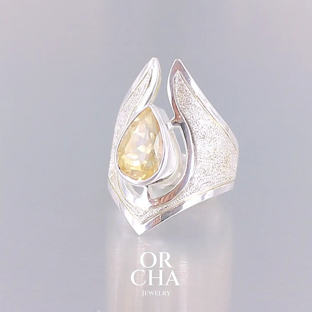 Grande bague contemporaine pour femme en argent massif sertie d'une Citrine. Pierre facettée en forme de goutte de qualité transparente, propre à l'oeil. Pierre naturelle de couleur jaune or lumineux. Bijoux unique, éthique et durable présenté dans un coffret de notre marque, prêt à offrir. Livraison offerte, certificat d'authenticité, service client.