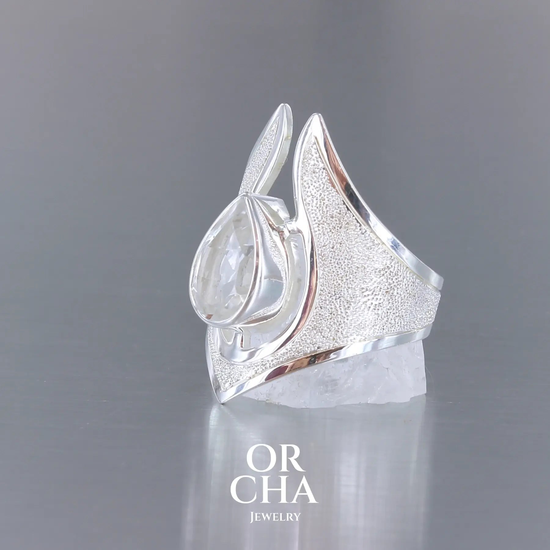Grande bague pour femme en argent massif sertie d'une Topaze blanche, collection Bastet. Pierre facettée en forme de goutte, pierre naturelle incolore avec un très bel éclat. Pierre fine de qualité transparente propre à l'oeil. Disponible en plusieurs tailles. Bijoux unique, éthique et durable présenté dans un coffret de notre marque, prêt à offrir. Livraison offerte, certificat d'authenticité, service client.