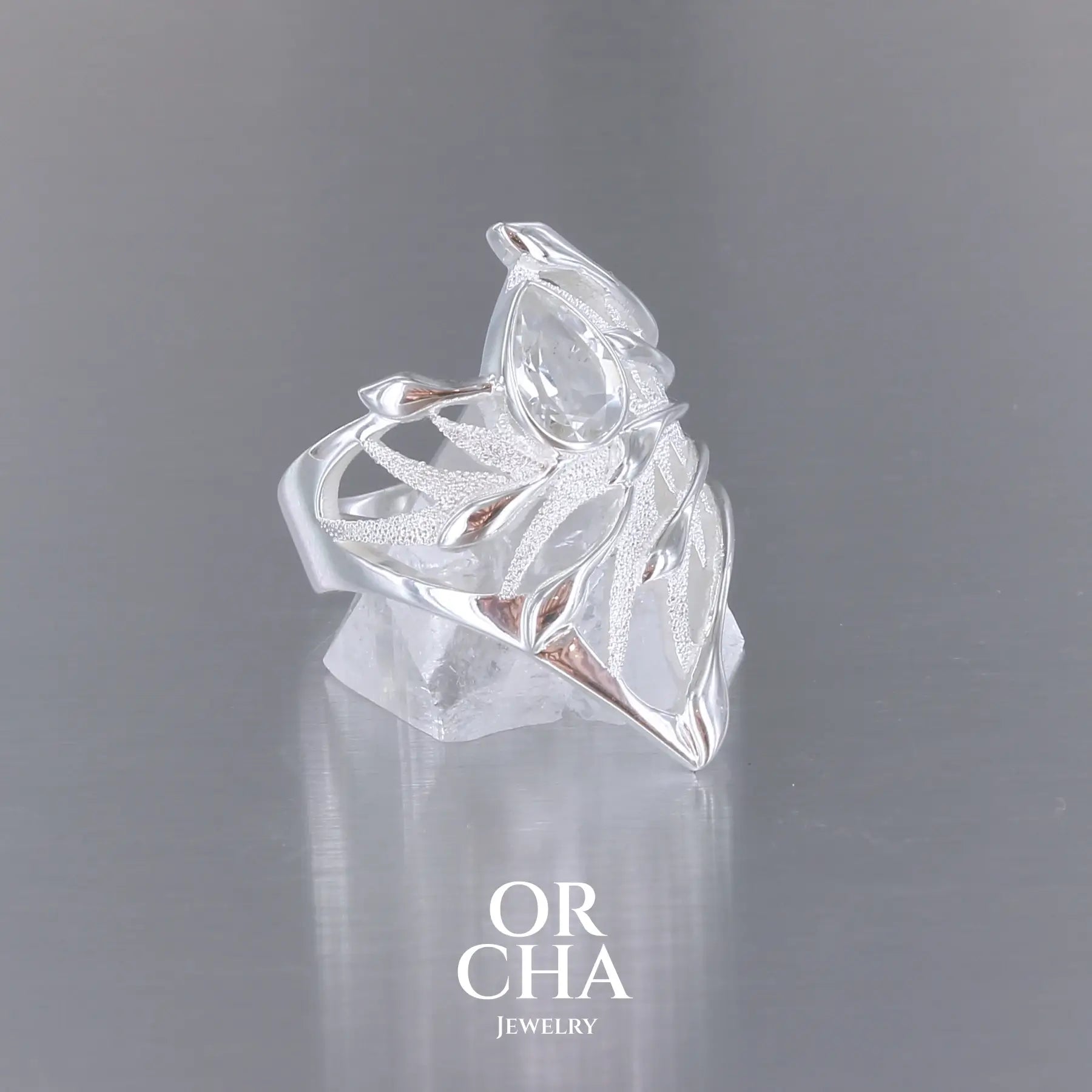 Grande Bague Jungle illustrant un feuillage tropicale, pour femme, en argent massif sertie d'une Topaze blanche facettée en forme de goutte. Pierre incolore, très lumineuse et propre à l'oeil. Disponible en plusieurs tailles. Bijoux unique, éthique et durable présenté dans un coffret de notre marque, prêt à offrir. Livraison offerte, certificat d'authenticité, service client.