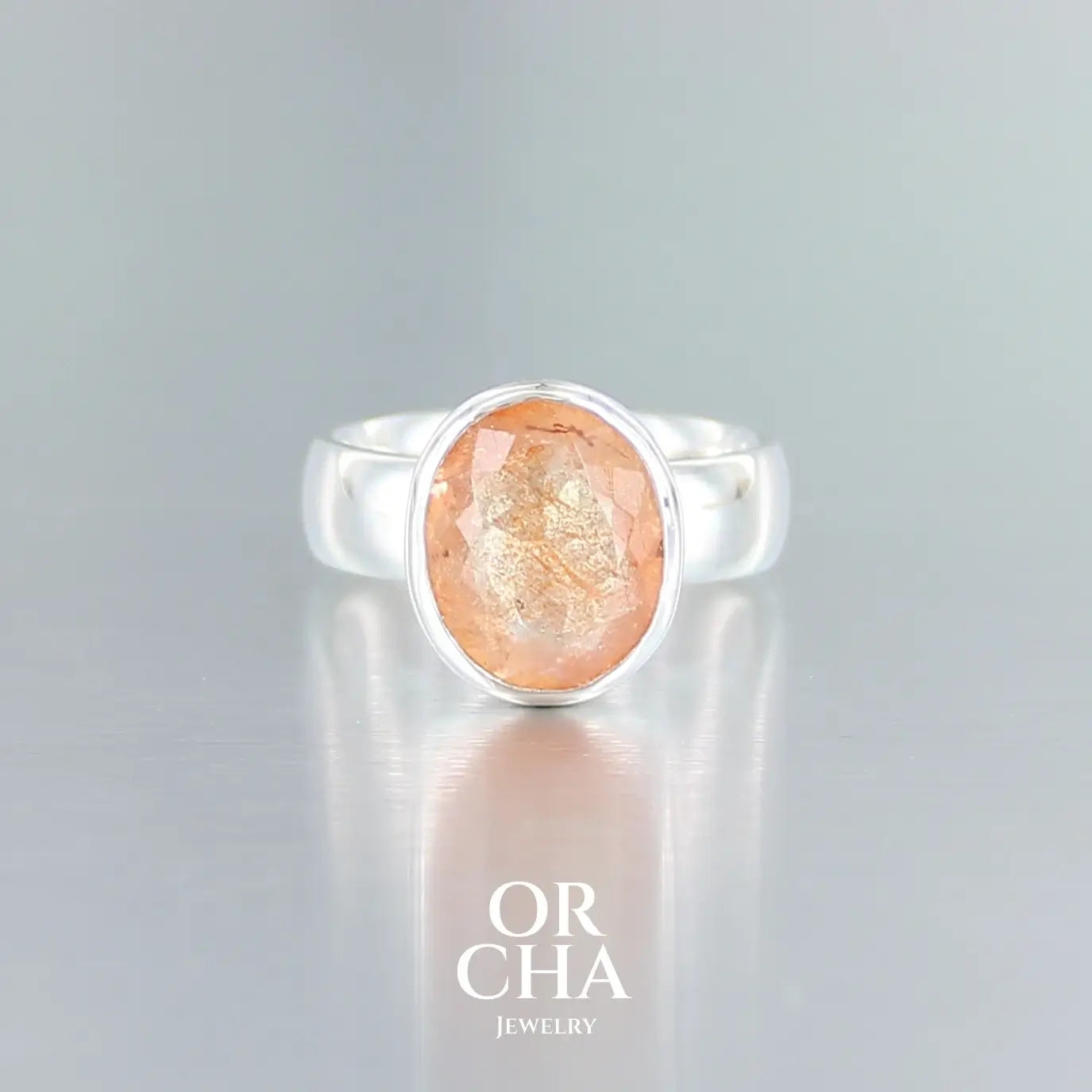 Bague de créateur en argent massif pour femme sertie d'une magnifique pierre de soleil. Pierre facettée de forme ovale de qualité transparente. Pierre naturelle de couleur orange à scintillement doré. Bague réalisée en taille 56. Bijoux unique, éthique et durable présenté dans un coffret de notre marque, prêt à offrir. Livraison offerte, certificat d'authenticité, service client.