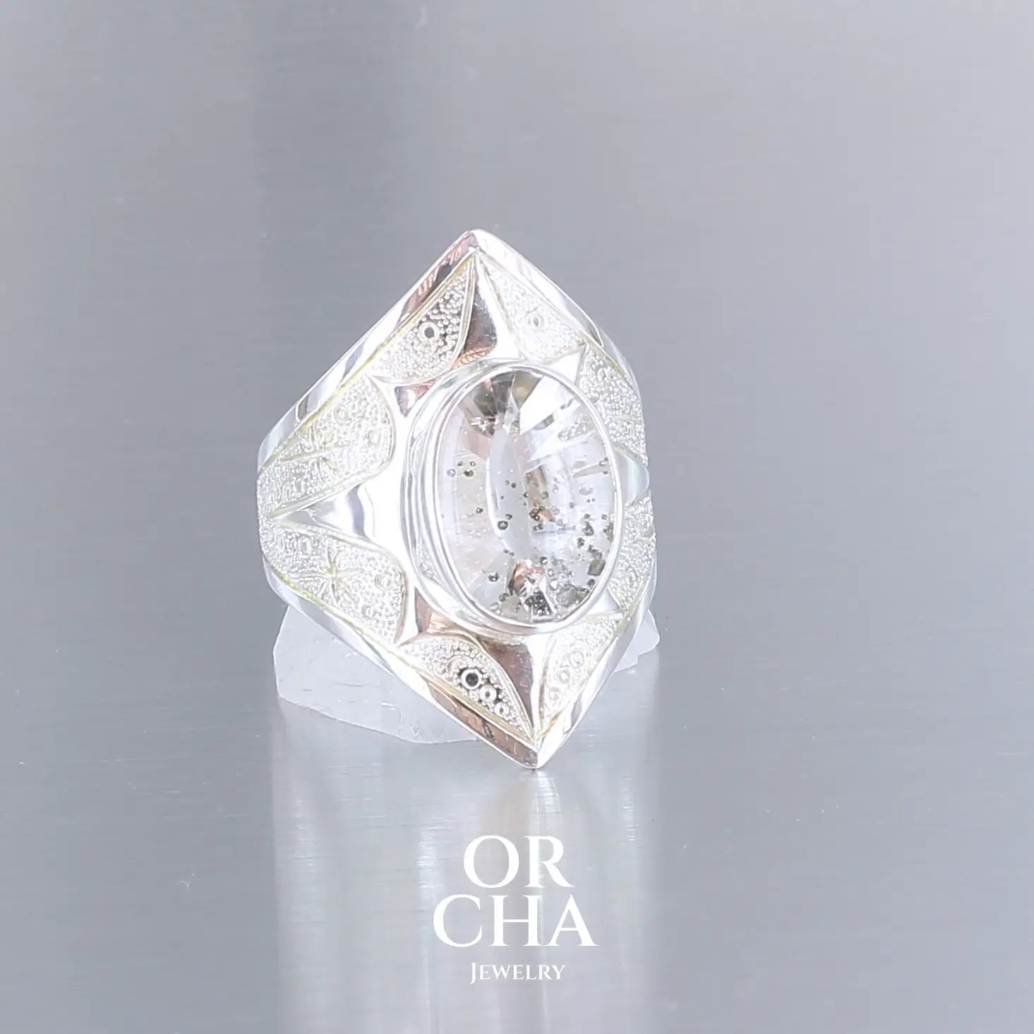 Bague pour femme en argent massif sculptées d'étoiles et autres corps célestes sertie d'un quartz à inclusions. Pierre cabochon de forme ovale, incolore avec inclusions dorés de pyrite de fer . Qualité transparentee, pierre naturelle. Taille 59. Bijoux unique, éthique et durable présenté dans un coffret de notre marque, prêt à offrir. Livraison offerte, certificat d'authenticité, service client.