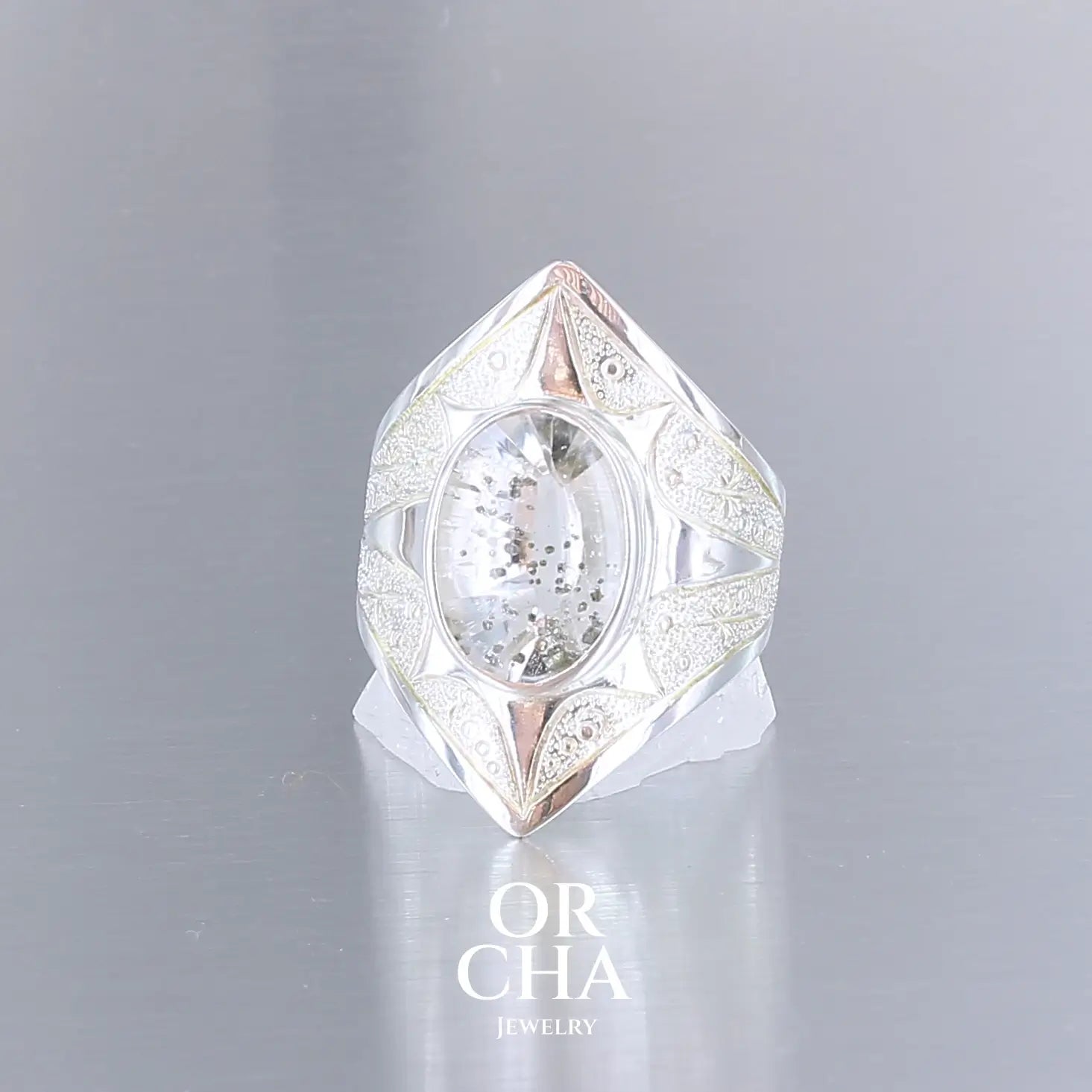 Bague pour femme en argent massif sculptées d'étoiles et autres corps célestes sertie d'un quartz à inclusions. Pierre cabochon de forme ovale, incolore avec inclusions dorés de pyrite de fer . Qualité transparentee, pierre naturelle. Taille 59. Bijoux unique, éthique et durable présenté dans un coffret de notre marque, prêt à offrir. Livraison offerte, certificat d'authenticité, service client.