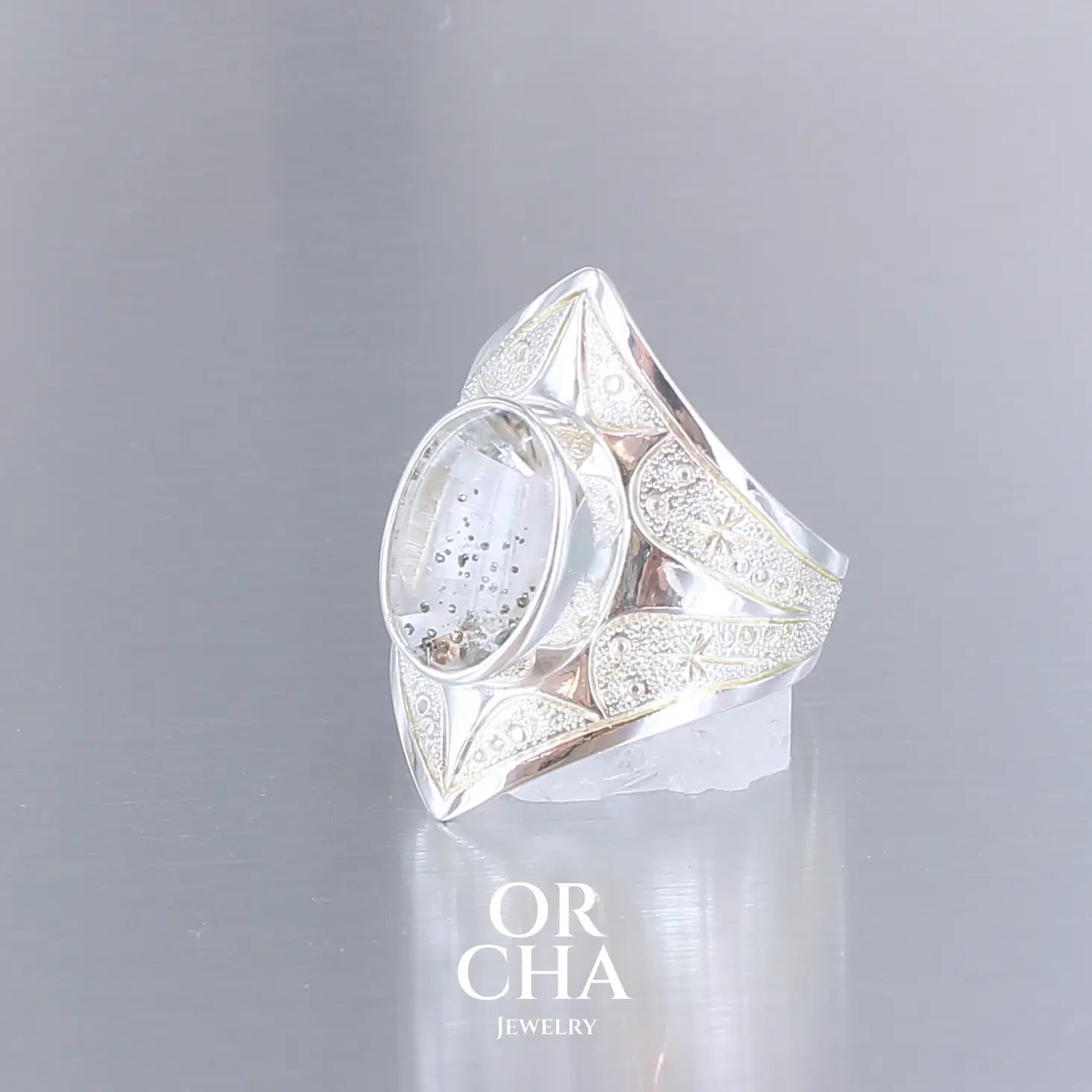 Bague pour femme en argent massif sculptées d'étoiles et autres corps célestes sertie d'un quartz à inclusions. Pierre cabochon de forme ovale, incolore avec inclusions dorés de pyrite de fer . Qualité transparentee, pierre naturelle. Taille 59. Bijoux unique, éthique et durable présenté dans un coffret de notre marque, prêt à offrir. Livraison offerte, certificat d'authenticité, service client.