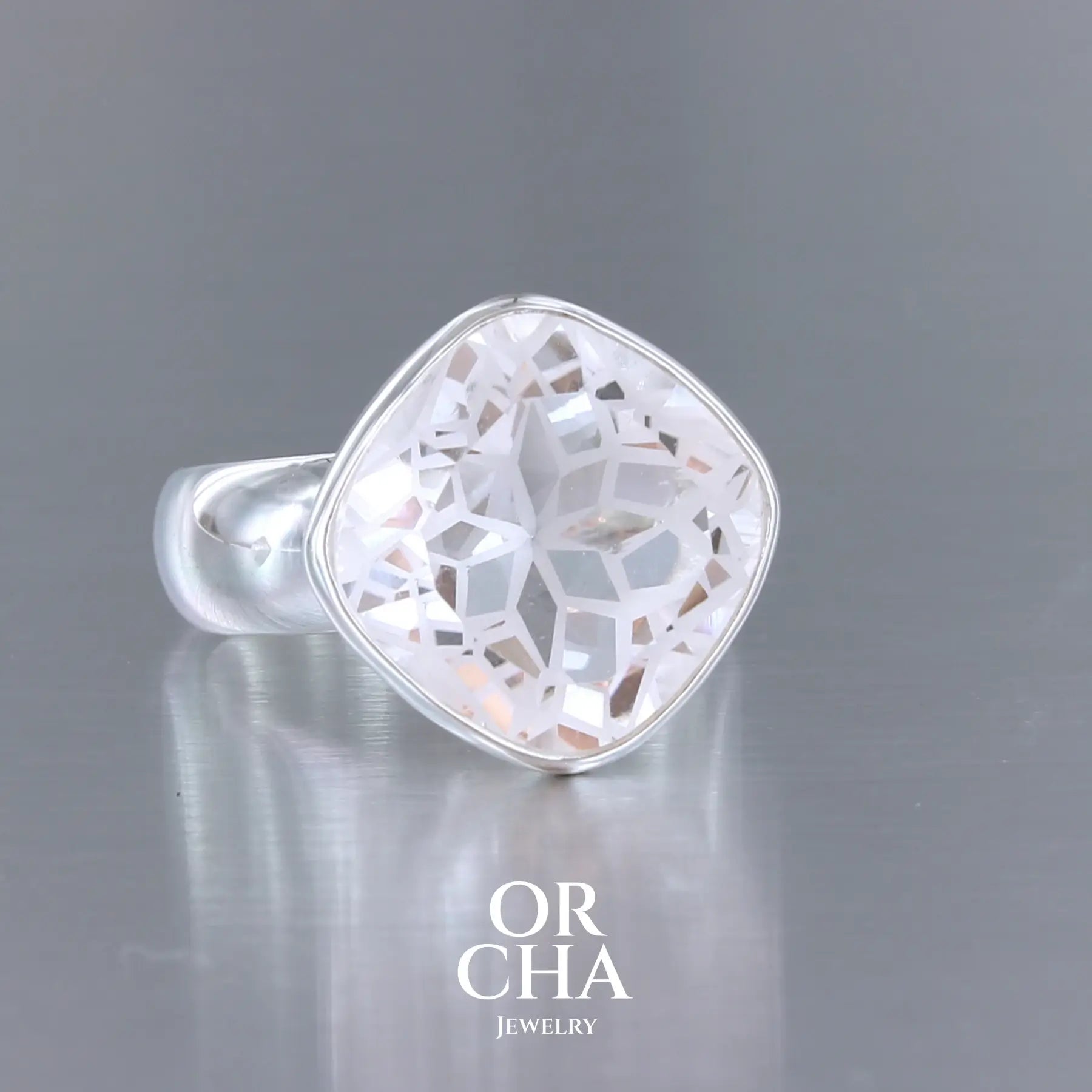 Bague cocktail pour femme en argent massif sertie d'un Cristal de roche gravé d'une fleur de vie. Pierre facettée de forme carrée de qualité transparente, propre à l'oeil. Pierre naturelle incolore et blanche sur les parties gravées. Bague réalisée en taille 60. Bijoux unique, éthique et durable présenté dans un coffret de notre marque, prêt à offrir. Livraison offerte, certificat d'authenticité, service client.