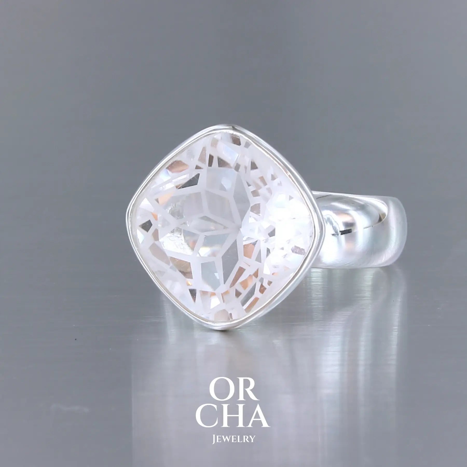 Bague cocktail pour femme en argent massif sertie d'un Cristal de roche gravé d'une fleur de vie. Pierre facettée de forme carrée de qualité transparente, propre à l'oeil. Pierre naturelle incolore et blanche sur les parties gravées. Bague réalisée en taille 60. Bijoux unique, éthique et durable présenté dans un coffret de notre marque, prêt à offrir. Livraison offerte, certificat d'authenticité, service client.