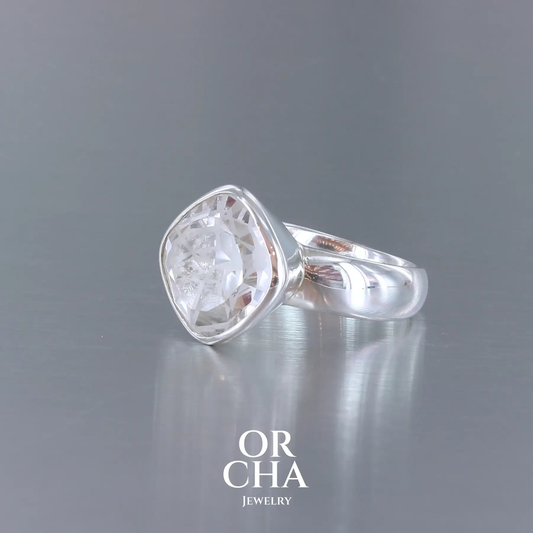 Bague cocktail pour femme en argent massif sertie d'un Cristal de roche gravé d'une fleur de vie. Pierre facettée de forme carrée de qualité transparente, propre à l'oeil. Pierre naturelle incolore et blanche sur les parties gravées. Bague réalisée en taille 52 ou 54. Bijoux unique, éthique et durable présenté dans un coffret de notre marque, prêt à offrir. Livraison offerte, certificat d'authenticité, service client.