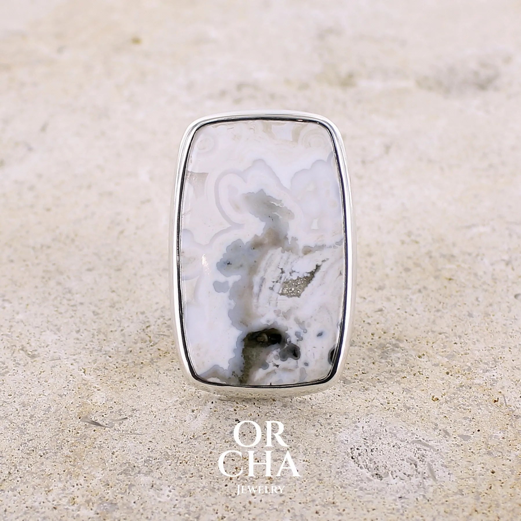 Bague pour femme en argent massif sertie d'un cabochon rectangulaire de jaspe océan de couleur blanc crème, gris, kaki et beige. Pierre de qualité opaque. Bijou unique réalisée en taille 54 par Orchajewelry