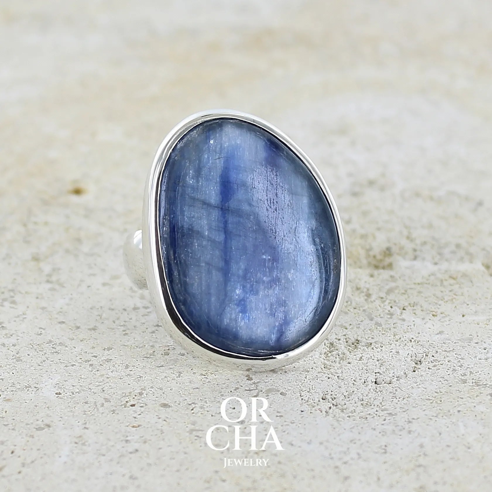 Bague pour femme en argent massif sertie d'un cabochon de cyanite de couleur bleu jean nacré. Pierre translucide à inclusions. Bijou unique réalisée en taille 55 par Orcha Jewelry