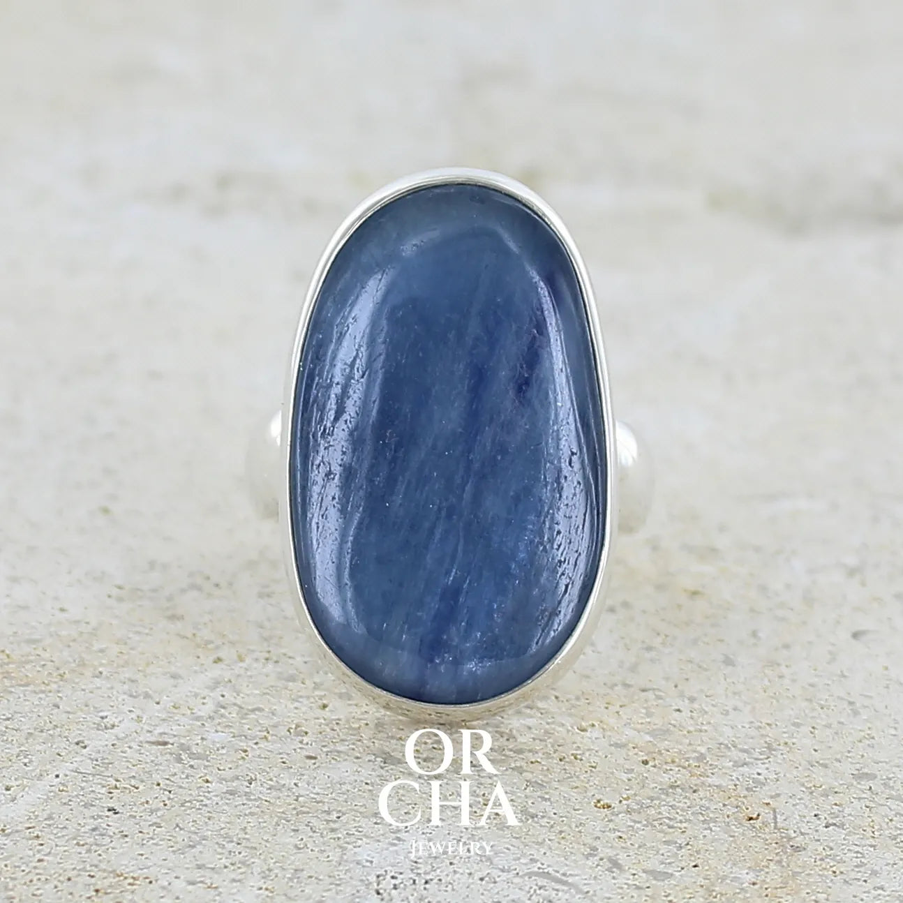 Bague pour femme en argent massif sertie d'un cabochon de cyanite de couleur bleu jean nacré. Pierre translucide à inclusions de forme ovale arrondie. Bijou unique réalisée en taille 58,5 par Orchajewelry