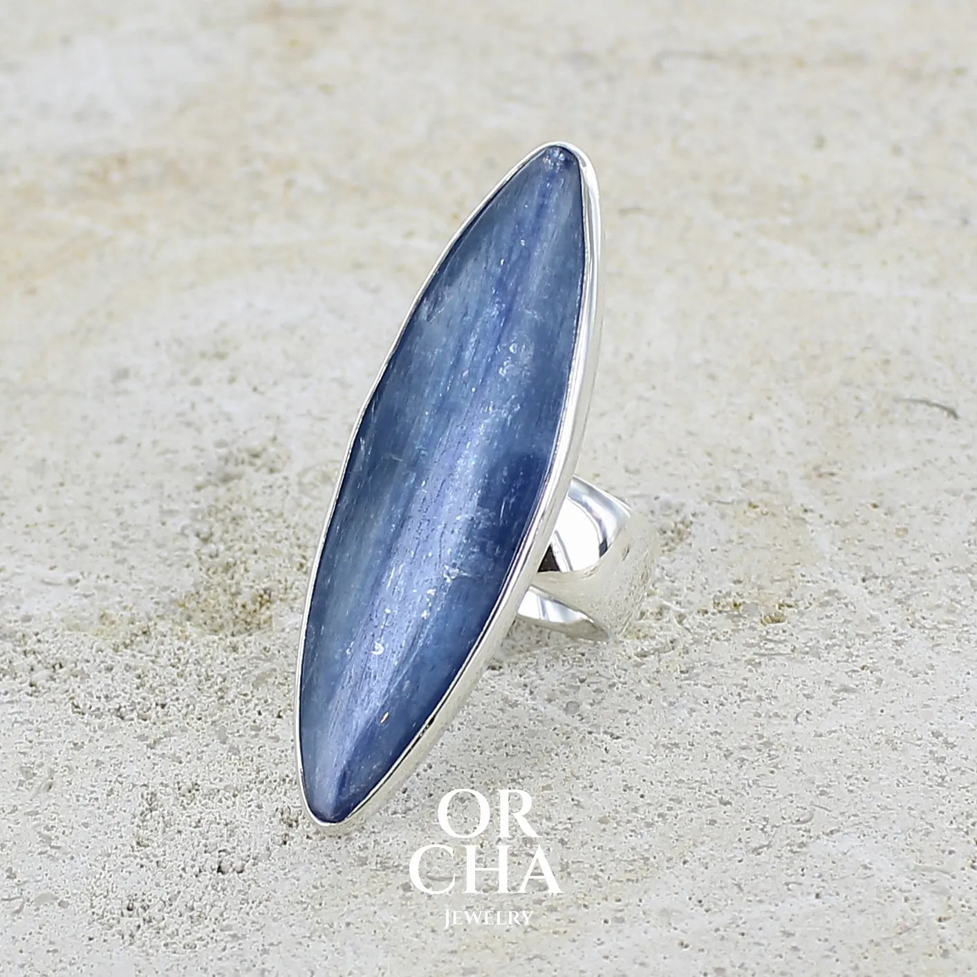 Bague marquise pour femme en argent massif sertie d'un cabochon de cyanite de couleur bleu jean nacré. Pierre translucide à inclusions. Bijou unique réalisée en taille 58 par Orchajewelry