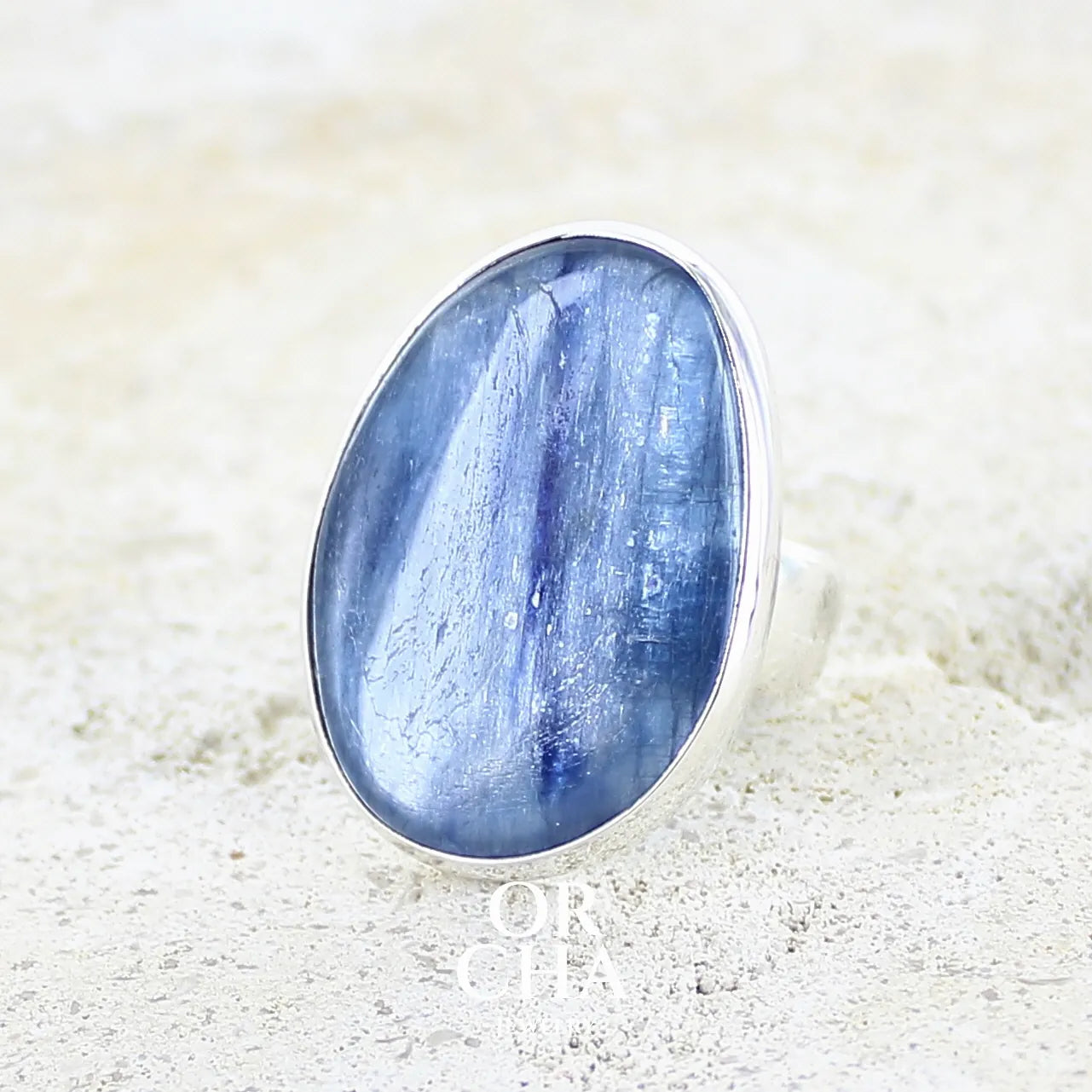 Bague pour femme en argent massif sertie d'un cabochon de cyanite de couleur bleu jean irisée. Pierre translucide à inclusions. Bijou unique réalisée en taille 56 par Orcha Jewelry
