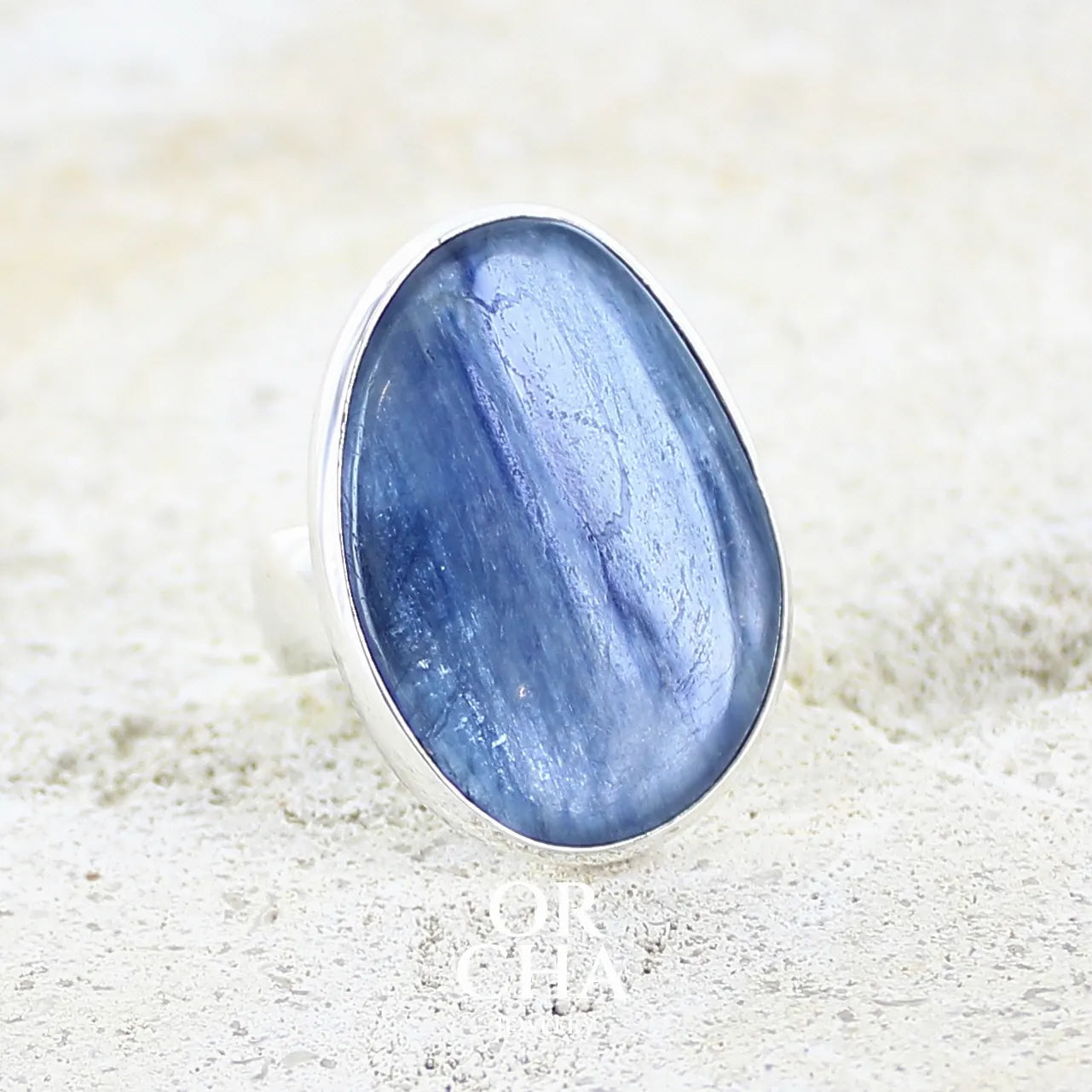 Bague pour femme en argent massif sertie d'un cabochon de cyanite de couleur bleu jean irisée. Pierre translucide à inclusions. Bijou unique réalisée en taille 56 par Orcha Jewelry