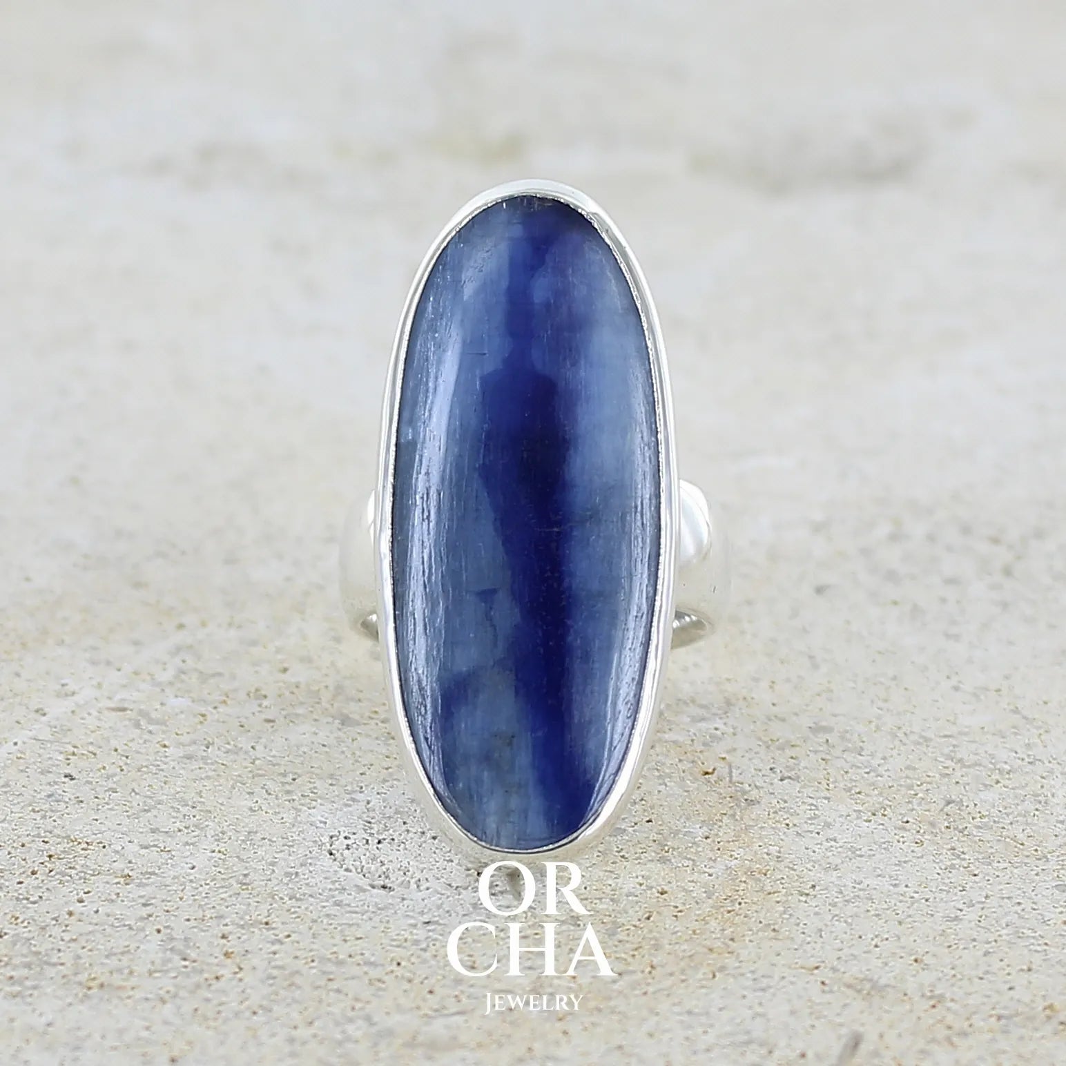 Bague pour femme en argent massif sertie d'un long cabochon ovale de cyanite bicolore de couleur bleu jean nacré. Pierre translucide à inclusions. Bijou unique réalisée en taille 54 par Orchajewelry