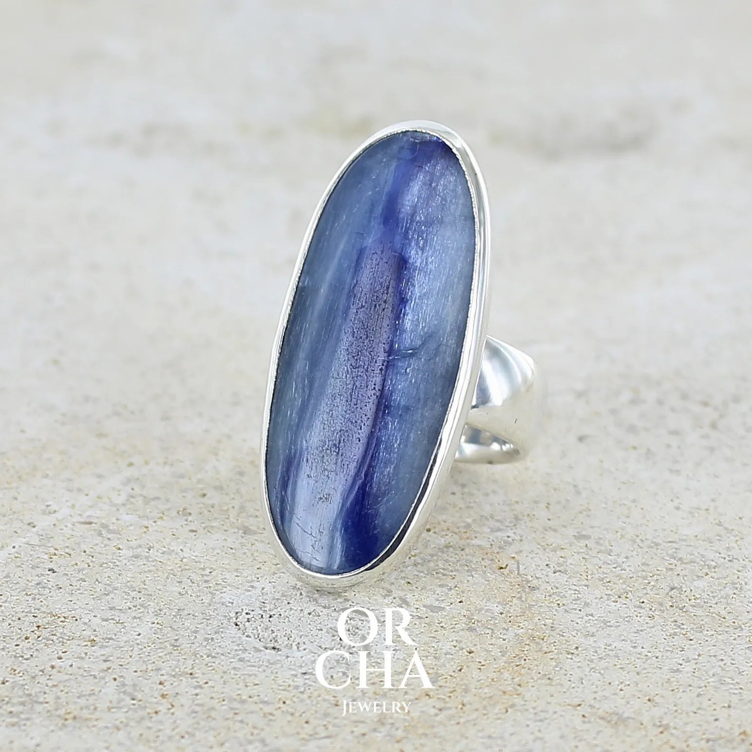 Bague pour femme en argent massif sertie d'un long cabochon ovale de cyanite bicolore de couleur bleu jean nacré. Pierre translucide à inclusions. Bijou unique réalisée en taille 54 par Orchajewelry