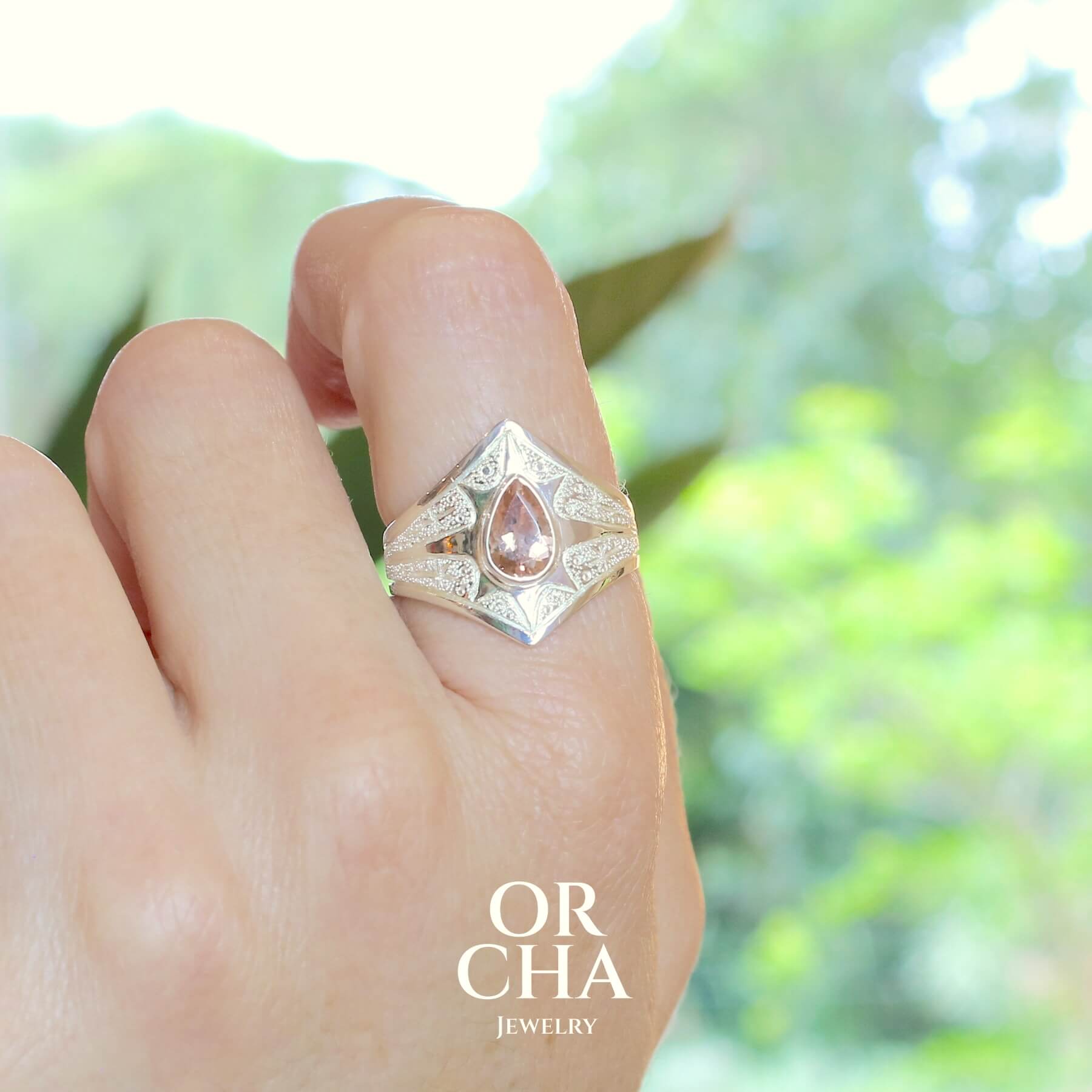 Bague pour femme en argent massif sculptées d'étoiles et autres corps célestes sertie d'une Tourmaline rose pêche. Pierre facettée en forme de goutte, de qualité transparente propre à l'oeil. Taille 61. Bijoux unique, éthique et durable présenté dans un coffret de notre marque, prêt à offrir. Livraison offerte, certificat d'authenticité, service client.