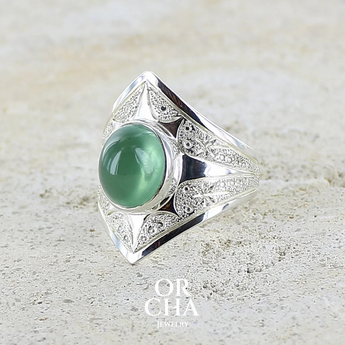 Bague pour femme en argent massif sculptées d'étoiles et autres corps célestes sertie d'un cabochon ovale de préhnite de couleur verte pastel lumineuse. Pierre naturelle de qualité transparente présentant des inclusions. Bijoux unique réalisé en taille 57 par Orchajewelry.