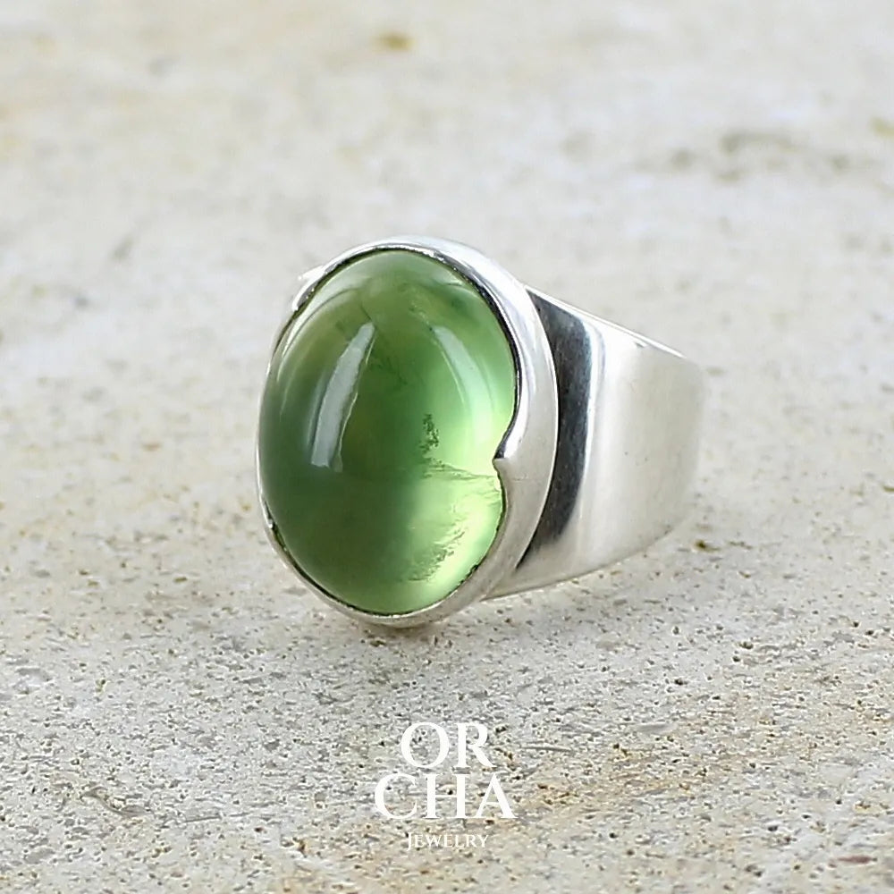 Bague pour femme en argent massif sertie d'une préhnite de couleur verte jaune clair. Pierre ovale taillée en cabochon. Pierre gemme de qualité transparente à inclusions. Bijoux unique réalisé en taille 52 par Orchajewelry.