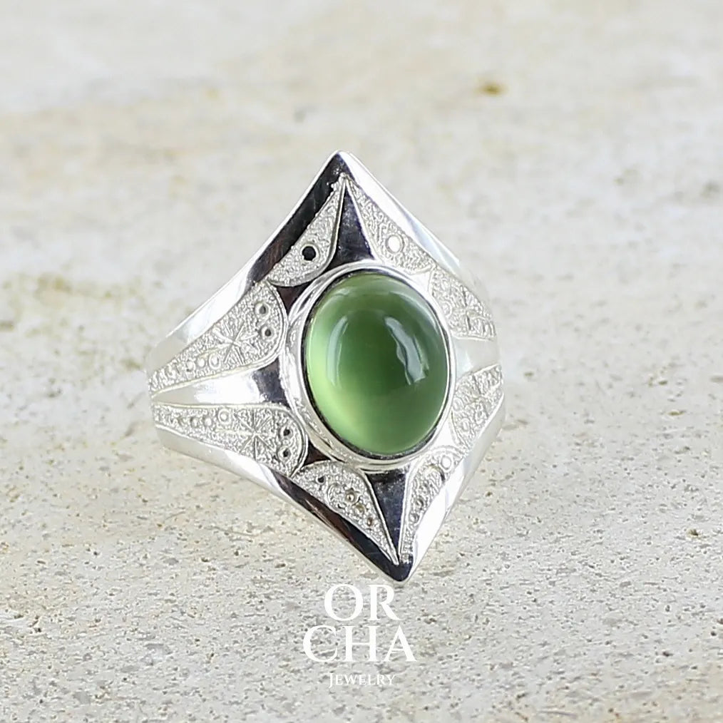 Bague pour femme en argent massif sculptées d'étoiles et autres corps célestes sertie d'un cabochon ovale de préhnite de couleur verte pastel lumineuse. Pierre naturelle de qualité transparente présentant des inclusions. Bijoux unique réalisé en taille 54,5 par Orchajewelry.