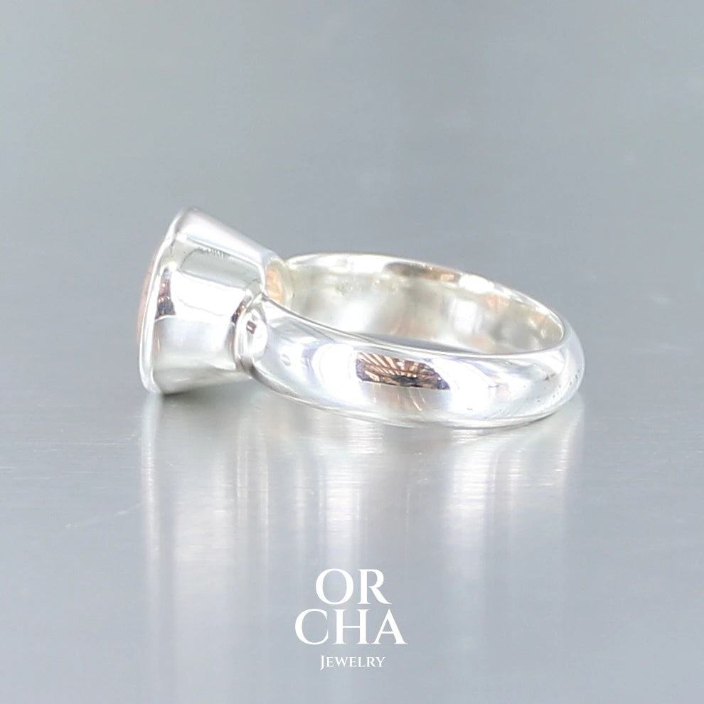Bague cocktail pour femme en argent massif sertie d'une Pierre de soleil. Pierre ovale facettée de de couleur orange clair avec des inclusions scintillantes d'hématites. Pierre naturelle. Bijoux unique, réalisé en taille 60, éthique et durable présenté dans un coffret de notre marque, prêt à offrir. Livraison offerte, certificat d'authenticité, service client.