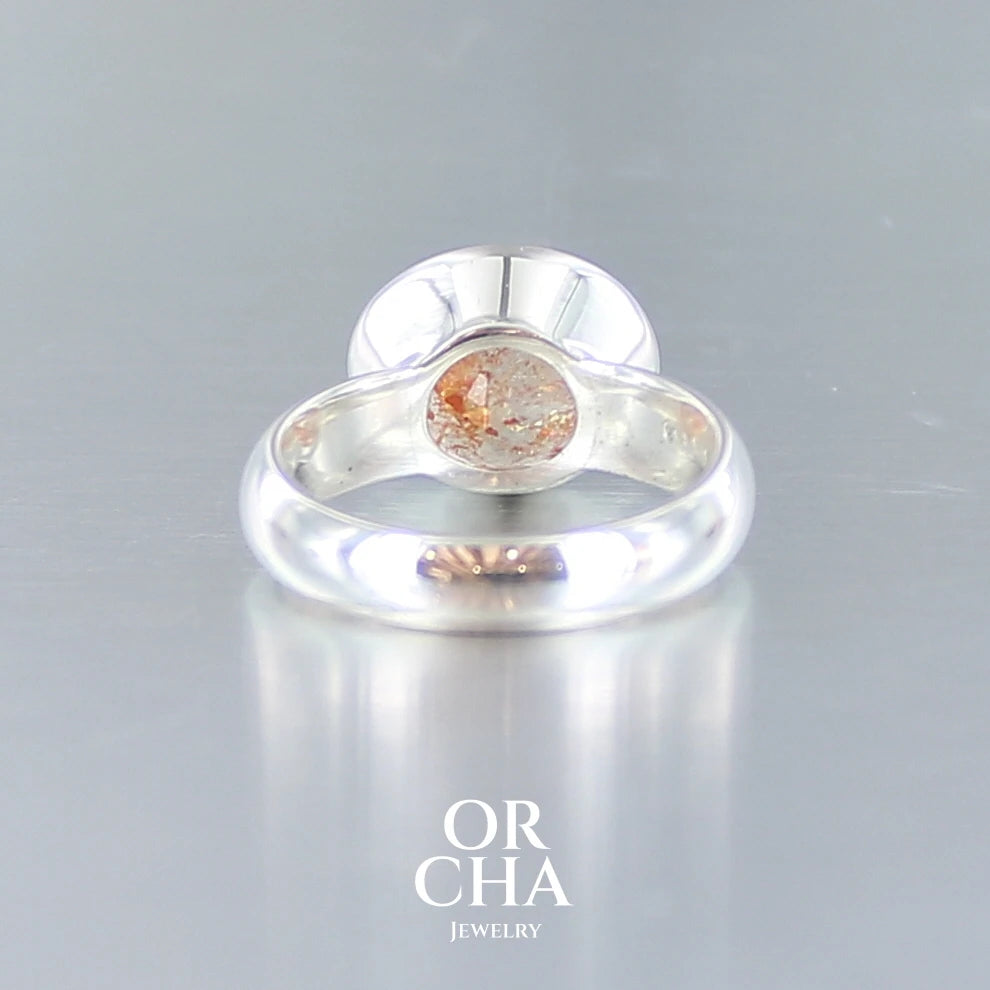 Bague cocktail pour femme en argent massif sertie d'une Pierre de soleil. Pierre ovale facettée de de couleur orange clair avec des inclusions scintillantes d'hématites. Pierre naturelle. Bijoux unique, réalisé en taille 60, éthique et durable présenté dans un coffret de notre marque, prêt à offrir. Livraison offerte, certificat d'authenticité, service client.