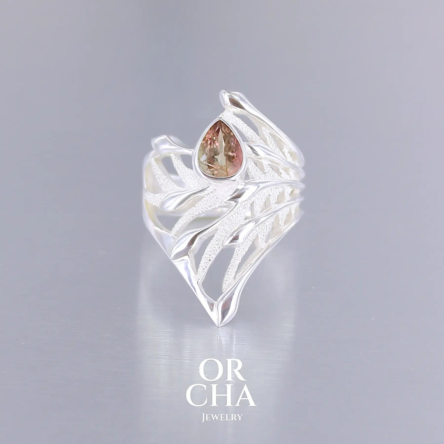 Grande Bague pour femme, feuillage tropicale travaillé en filigrane en argent massif, sertie d'une Tourmaline bicolore rose pêche et verte kaki. Pierre facettée en forme de goutte. Pierre incolore, très lumineuse et propre à l'oeil. Taille 56. Bijoux unique, éthique et durable présenté dans un coffret de notre marque, prêt à offrir. Livraison offerte, certificat d'authenticité, service client.