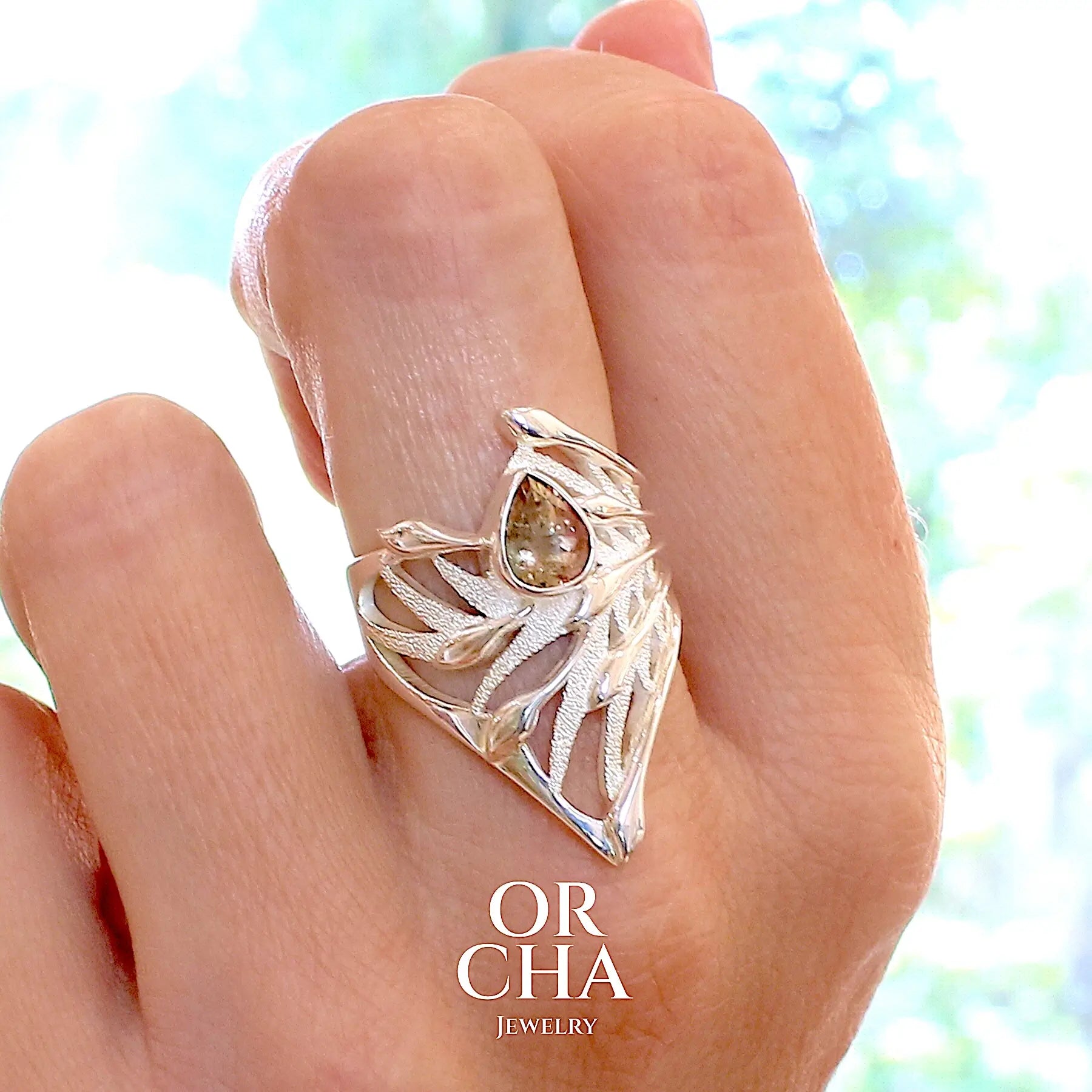 photo sur modèle d'une grande Bague pour femme, feuillage tropicale travaillé en filigrane en argent massif, sertie d'une Tourmaline bicolore rose pêche et verte kaki. Pierre facettée en forme de goutte. Pierre incolore, très lumineuse et propre à l'oeil. Taille 56. Bijoux unique, éthique et durable présenté dans un coffret de notre marque, prêt à offrir. Livraison offerte, certificat d'authenticité, service client.