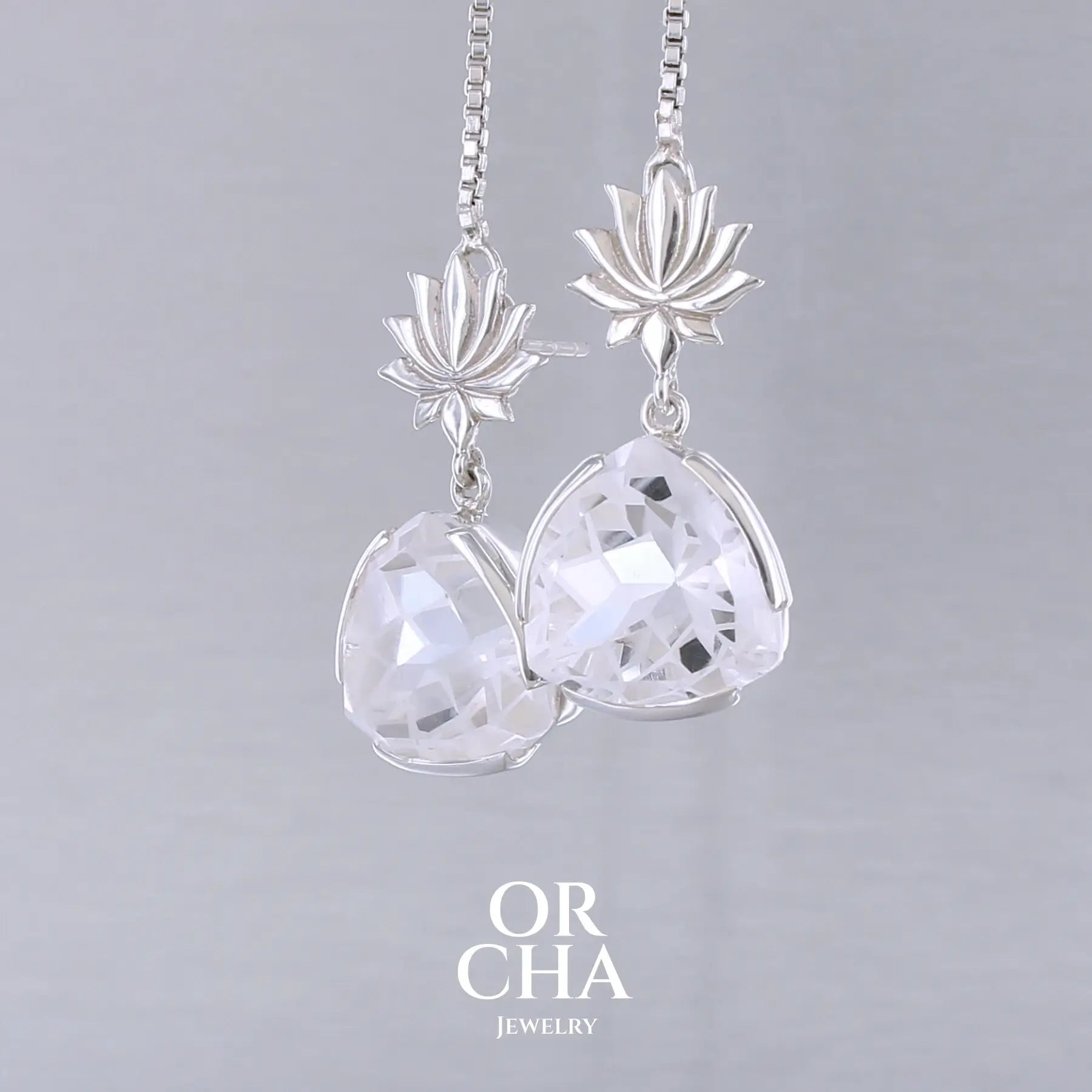 Boucles d'oreilles pour femme en argent massif sertie de Cristals de roche gravés de fleurs de vie. Pierres facettées de forme triangulaire de qualités transparentes, propre à l'oeil. Pierre naturelle incolore et blanche sur les parties gravées. Le clou des boucles représente un lotus. Bijoux unique, éthique et durable présenté dans un coffret de notre marque, prêt à offrir. Livraison offerte, certificat d'authenticité, service client.
