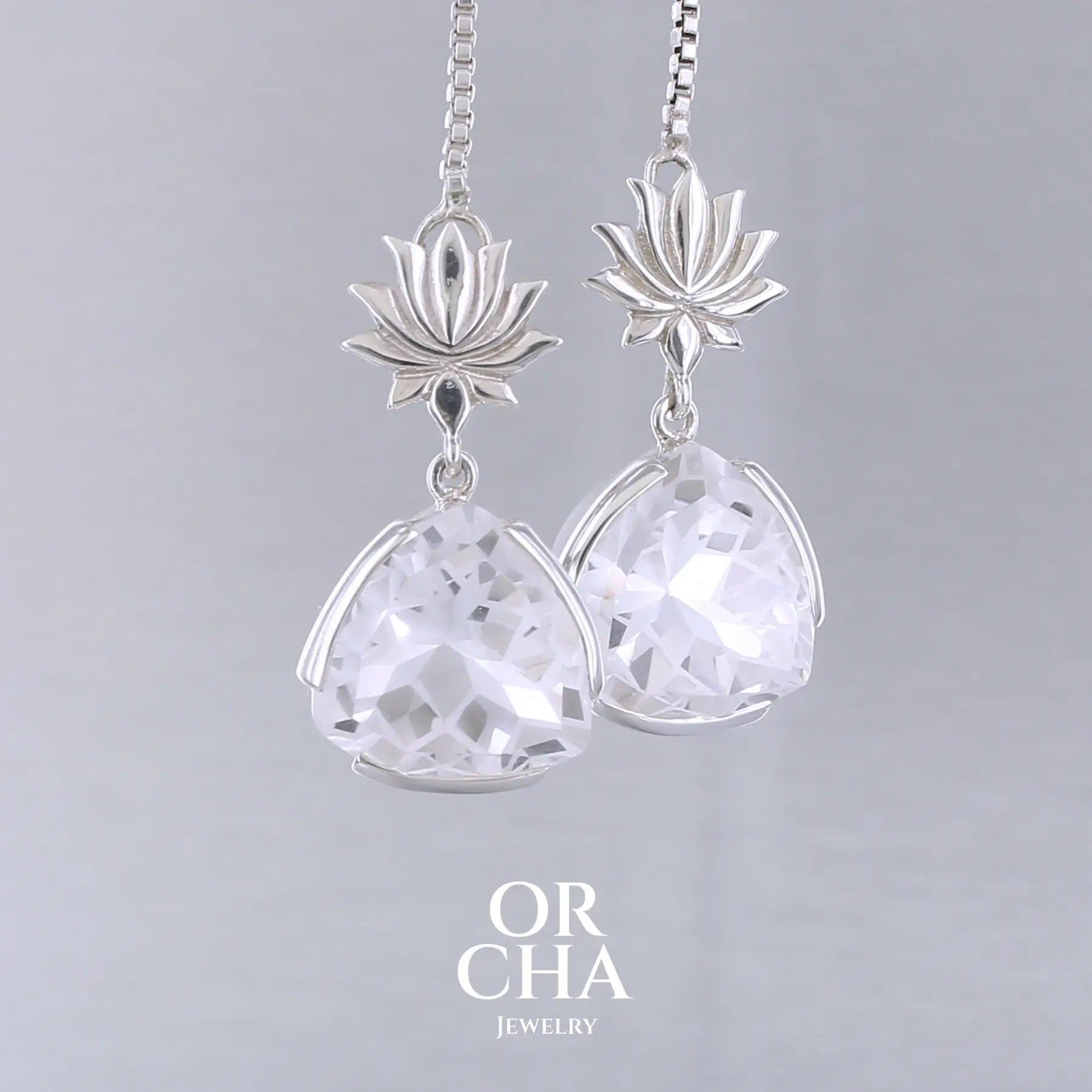 Boucles d'oreilles pour femme en argent massif sertie de Cristals de roche gravés de fleurs de vie. Pierres facettées de forme triangulaire de qualités transparentes, propre à l'oeil. Pierre naturelle incolore et blanche sur les parties gravées. Le clou des boucles représente un lotus. Bijoux unique, éthique et durable présenté dans un coffret de notre marque, prêt à offrir. Livraison offerte, certificat d'authenticité, service client.