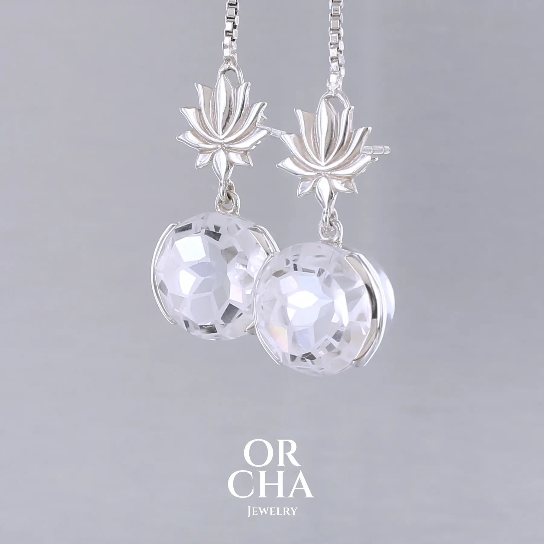 Boucles d'oreilles pour femme en argent massif sertie de Cristals de roche gravés de fleurs de vie. Pierres facettées de forme ronde de qualités transparentes, propre à l'oeil. Pierre naturelle incolore et blanche sur les parties gravées. Le clou des boucles représente un lotus. Bijoux unique, éthique et durable présenté dans un coffret de notre marque, prêt à offrir. Livraison offerte, certificat d'authenticité, service client.