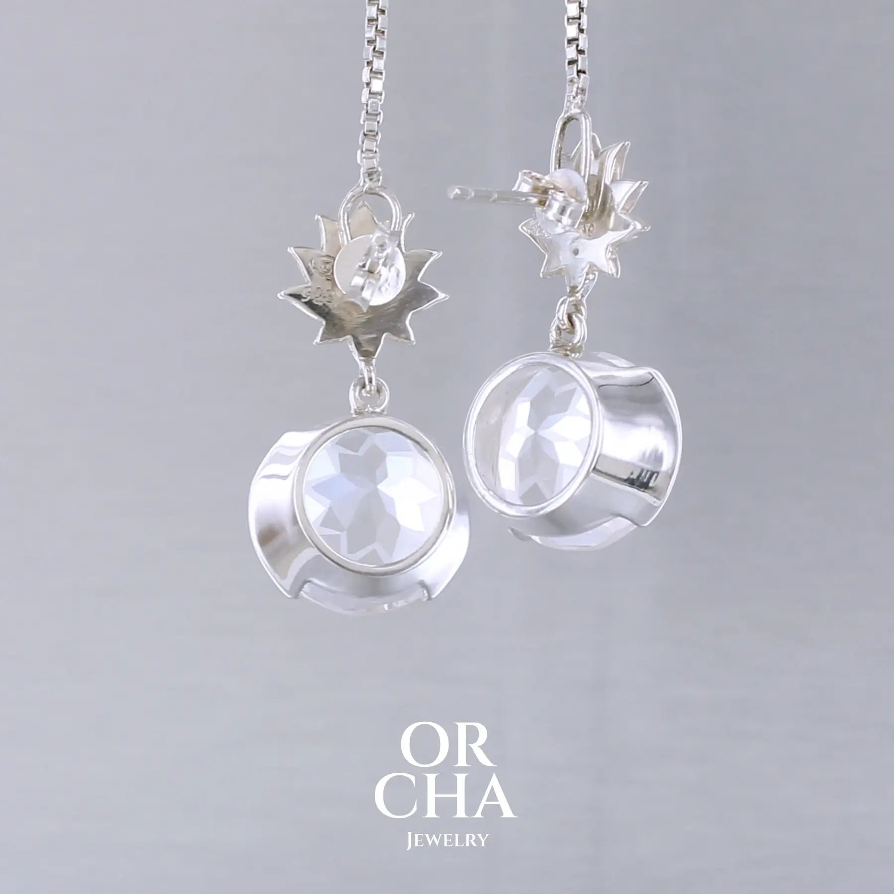 Boucles d'oreilles pour femme en argent massif sertie de Cristals de roche gravés de fleurs de vie. Pierres facettées de forme ronde de qualités transparentes, propre à l'oeil. Pierre naturelle incolore et blanche sur les parties gravées. Le clou des boucles représente un lotus. Bijoux unique, éthique et durable présenté dans un coffret de notre marque, prêt à offrir. Livraison offerte, certificat d'authenticité, service client.