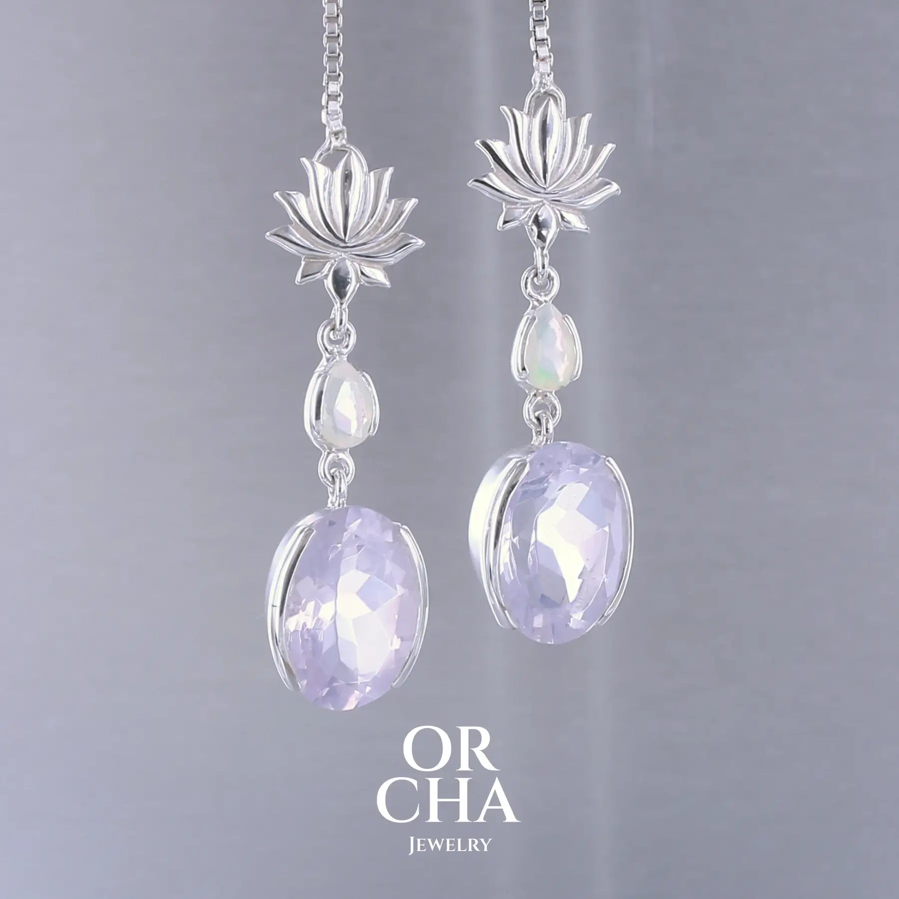 Boucles d'oreilles Lotus pour femme en argent massif sertie de Quartz lavandes et d'opales d'Éthiopie. Pierres facettées de forme ovales et de gouttes de qualités transparentes, propre à l'oeil. Pierres naturelles de couleurs violettes pastel teintées de rose avec des reflets opalescents et multicolores pour les opales . Bijoux unique, éthique et durable présenté dans un coffret de notre marque, prêt à offrir. Livraison offerte, certificat d'authenticité, service client.