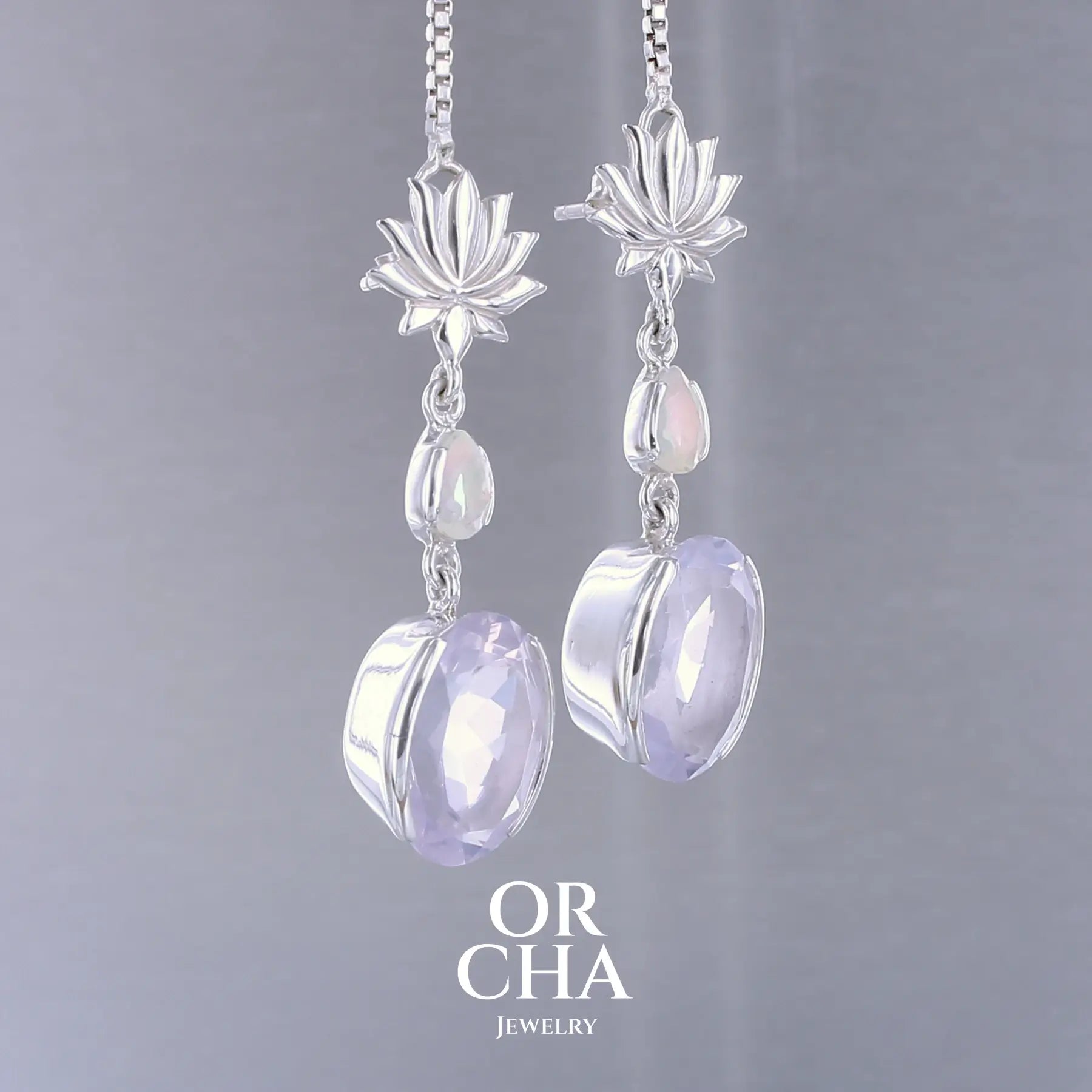 Boucles d'oreilles Lotus pour femme en argent massif sertie de Quartz lavandes et d'opales d'Éthiopie. Pierres facettées de forme ovales et de gouttes de qualités transparentes, propre à l'oeil. Pierres naturelles de couleurs violettes pastel teintées de rose avec des reflets opalescents et multicolores pour les opales . Bijoux unique, éthique et durable présenté dans un coffret de notre marque, prêt à offrir. Livraison offerte, certificat d'authenticité, service client.