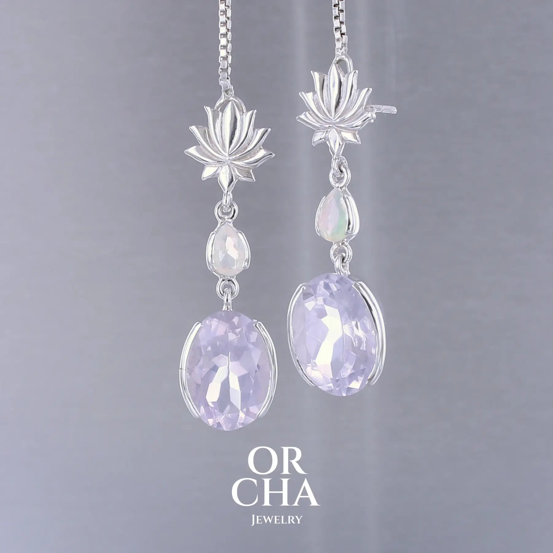 Boucles d'oreilles Lotus pour femme en argent massif sertie de Quartz lavandes et d'opales d'Éthiopie. Pierres facettées de forme ovales et de gouttes de qualités transparentes, propre à l'oeil. Pierres naturelles de couleurs violettes pastel teintées de rose avec des reflets opalescents et multicolores pour les opales . Bijoux unique, éthique et durable présenté dans un coffret de notre marque, prêt à offrir. Livraison offerte, certificat d'authenticité, service client.