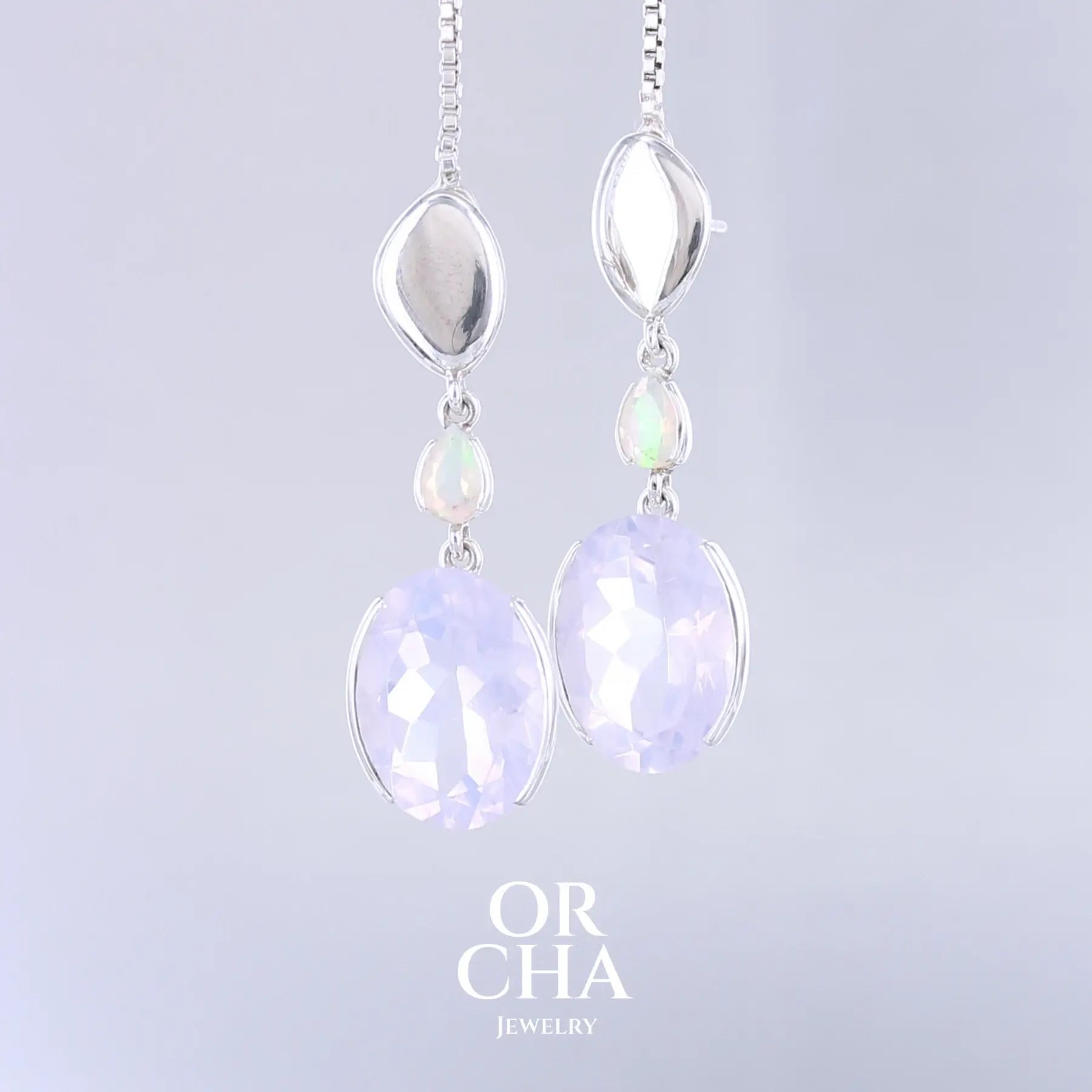 Boucles d'oreilles pour femme en argent massif sertie de Quartz lavandes et d'opales d'Éthiopie. Pierres facettées de forme ovales et de gouttes de qualités transparentes, propre à l'oeil. Pierres naturelles de couleurs violettes pastel teintées de rose avec des reflets opalescents et multicolores pour les opales . Bijoux unique, éthique et durable présenté dans un coffret de notre marque, prêt à offrir. Livraison offerte, certificat d'authenticité, service client.