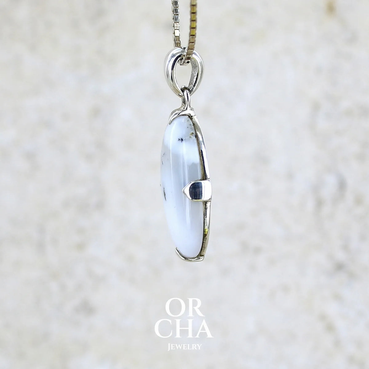 Détail du sertissage d'un pendentif pour femme en argent massif sertie d'un cabochon de forme ovale d'agate dendritique de couleur blanc pur et noir. Pierre opaque à translucide à inclusions paysages de dendrites de manganèse noires contrastées. Bijou unique réalisé par Orchajewelry