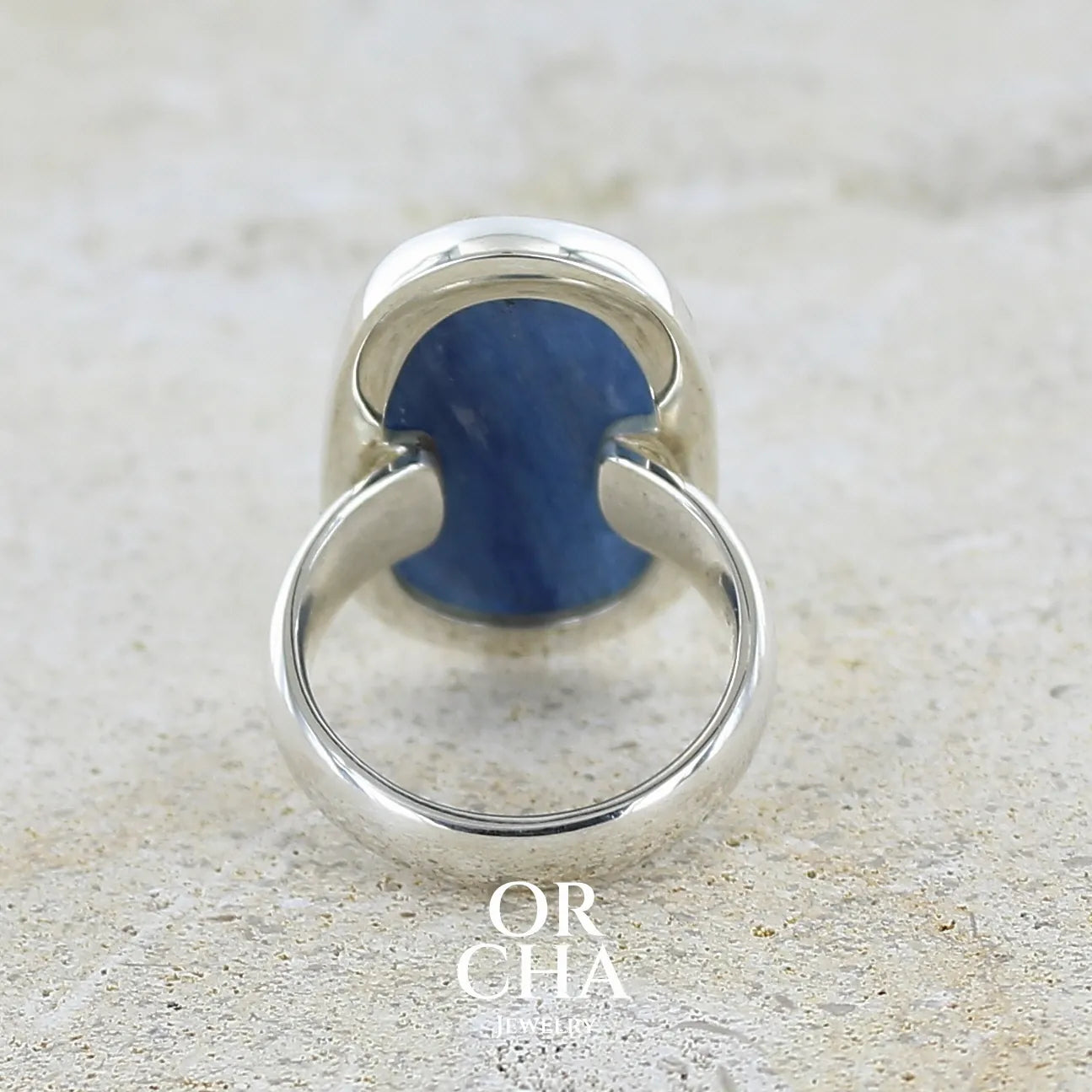 Vue de dos d'une bague pour femme en argent massif sertie d'un cabochon de cyanite de couleur bleu jean nacré. Pierre translucide à inclusions de forme ovale arrondie. Bijou unique réalisée en taille 58,5 par Orchajewelry