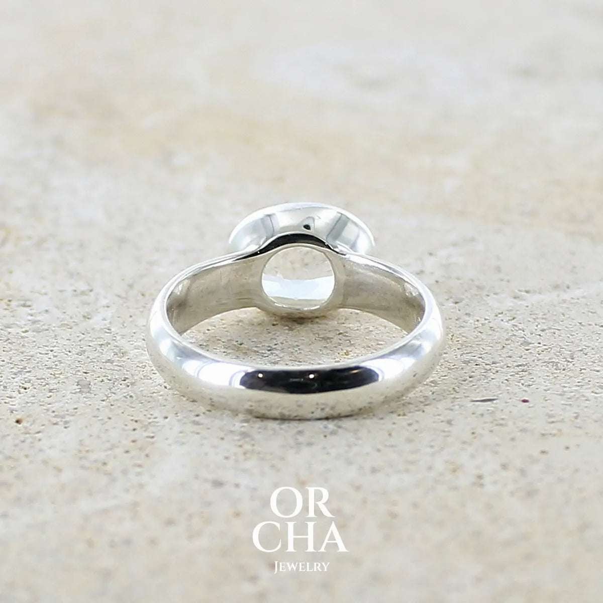 Vue de dos d'une bague cocktail pour femme en argent massif 925 sertie d'une pierre de lune de Madagascar taillée de 2,18 carats, pierre incolore aux reflets orangés et arc en ciel. Pierre transparente avec inclusions. Bijoux unique réalisé en taille 52 par Orcha Jewelry