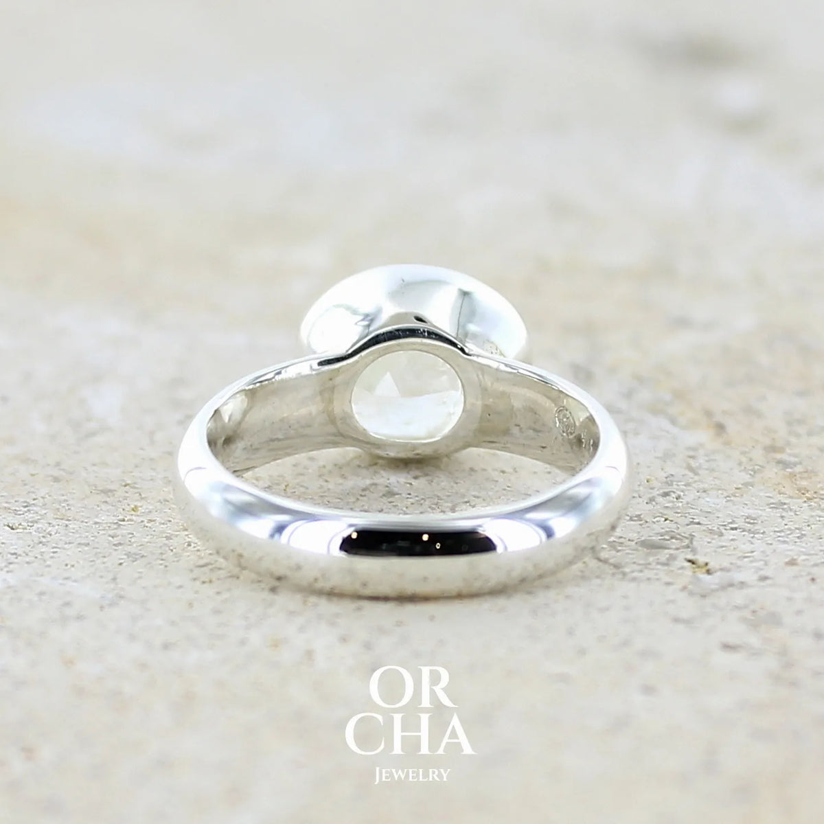 Vur de dos d'une bague cocktail pour femme en argent massif 925 sertie d'une pierre de lune arc en ciel de Madagascar taillée de 2,5 carats incolore aux reflets bleutés et arc en ciel. Pierre transparente avec inclusions. Bijoux unique réalisée en taille 56 par Orchajewelry