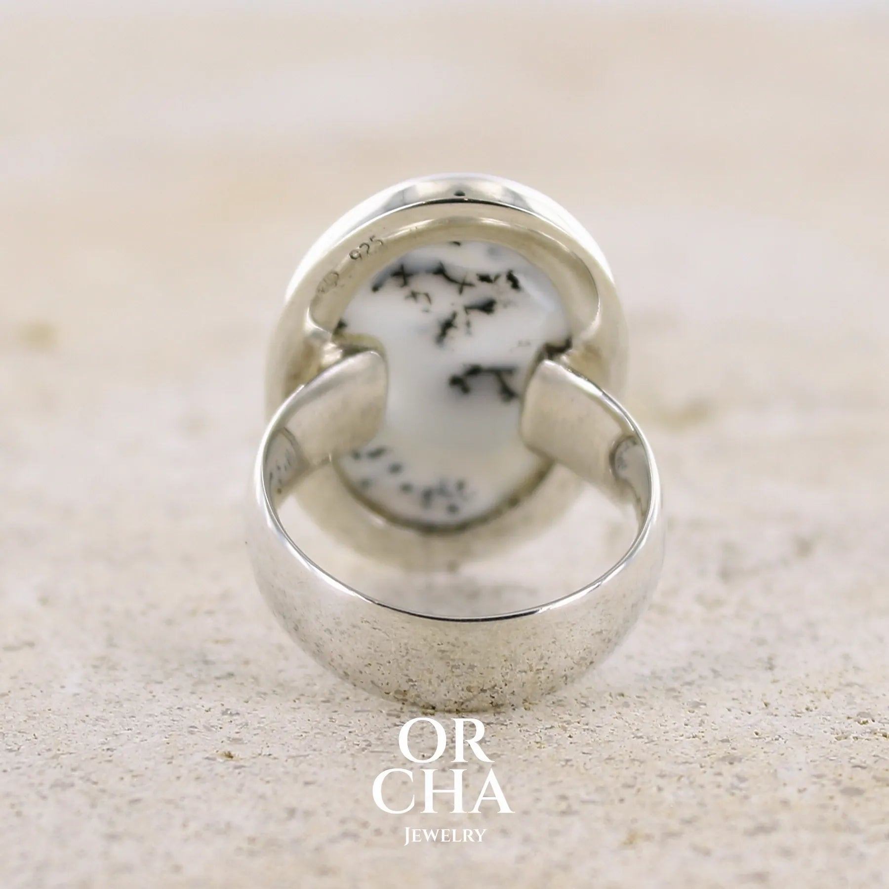 Vue de dos d'une bague pour femme en argent massif sertie d'un cabochon ovale d'agate dendritique de couleur blanc pur et noir. Pierre paysage opaque translucide à inclusions de dendrites de manganèse noires contrastées. Bijou unique réalisée en taille 52 par Orchajewelry