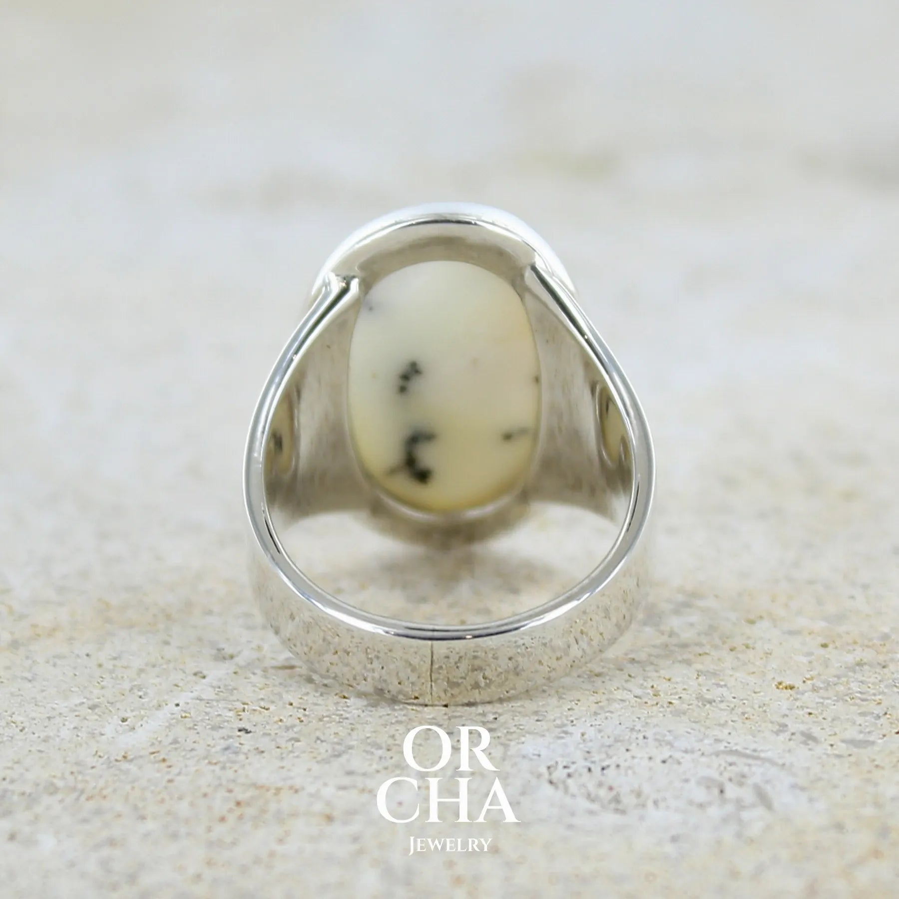Vue de dos d'une bague pour femme en argent massif sertie d'un cabochon ovale d'agate dendritique de couleur blanc pur et noir. Pierre opaque translucide à inclusions paysages de dendrites de manganèse noires contrastées. Bijou unique réalisé en taille 54 par Orchajewelry