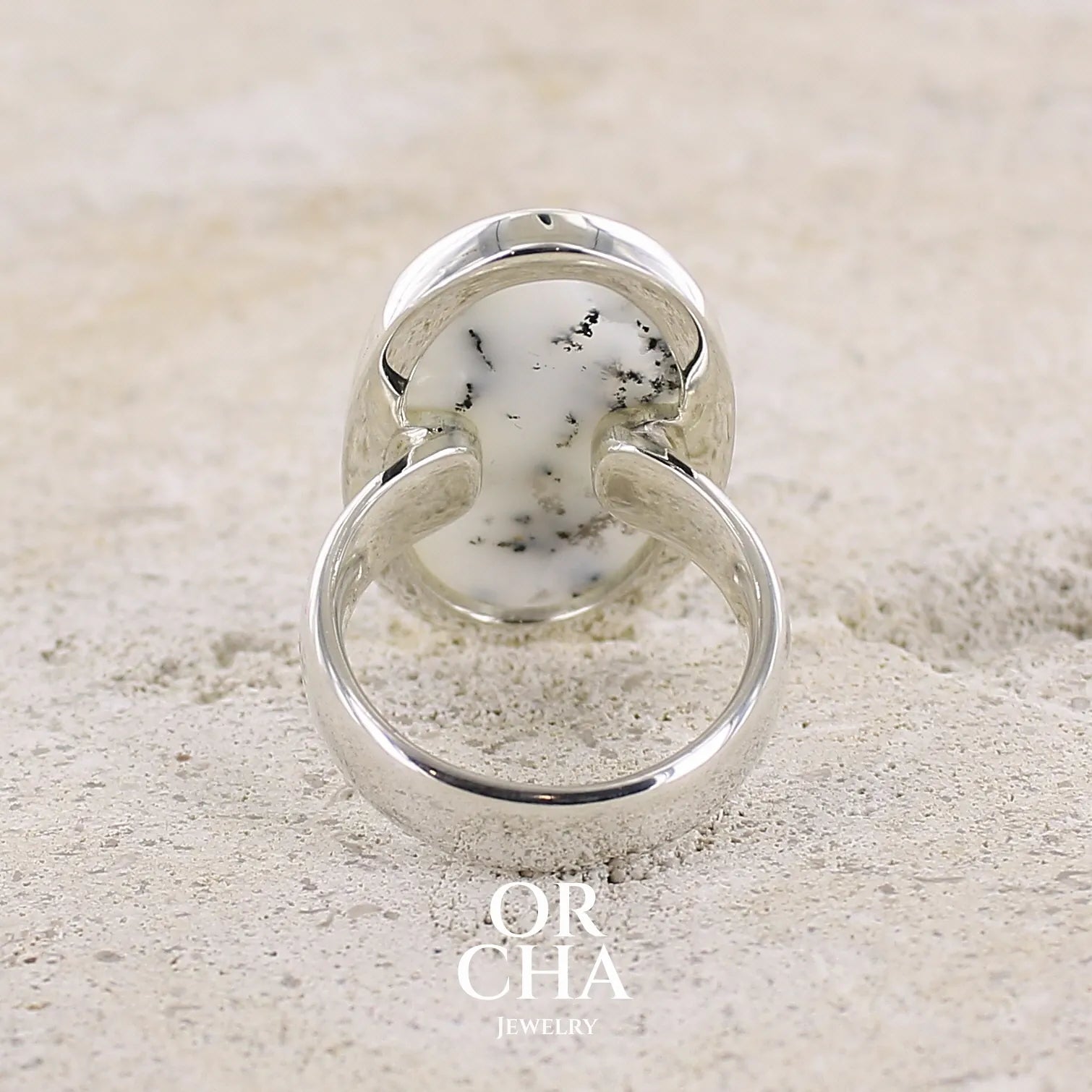 Vue de dos d'une bague pour femme en argent massif sertie d'un cabochon d'agate dendritique de couleur blanche et noire. Pierre de forme ovale de qualité translucide à inclusions paysages de manganèse contrastées. Bijou unique réalisée en taille 58,5 par Orcha Jewelry