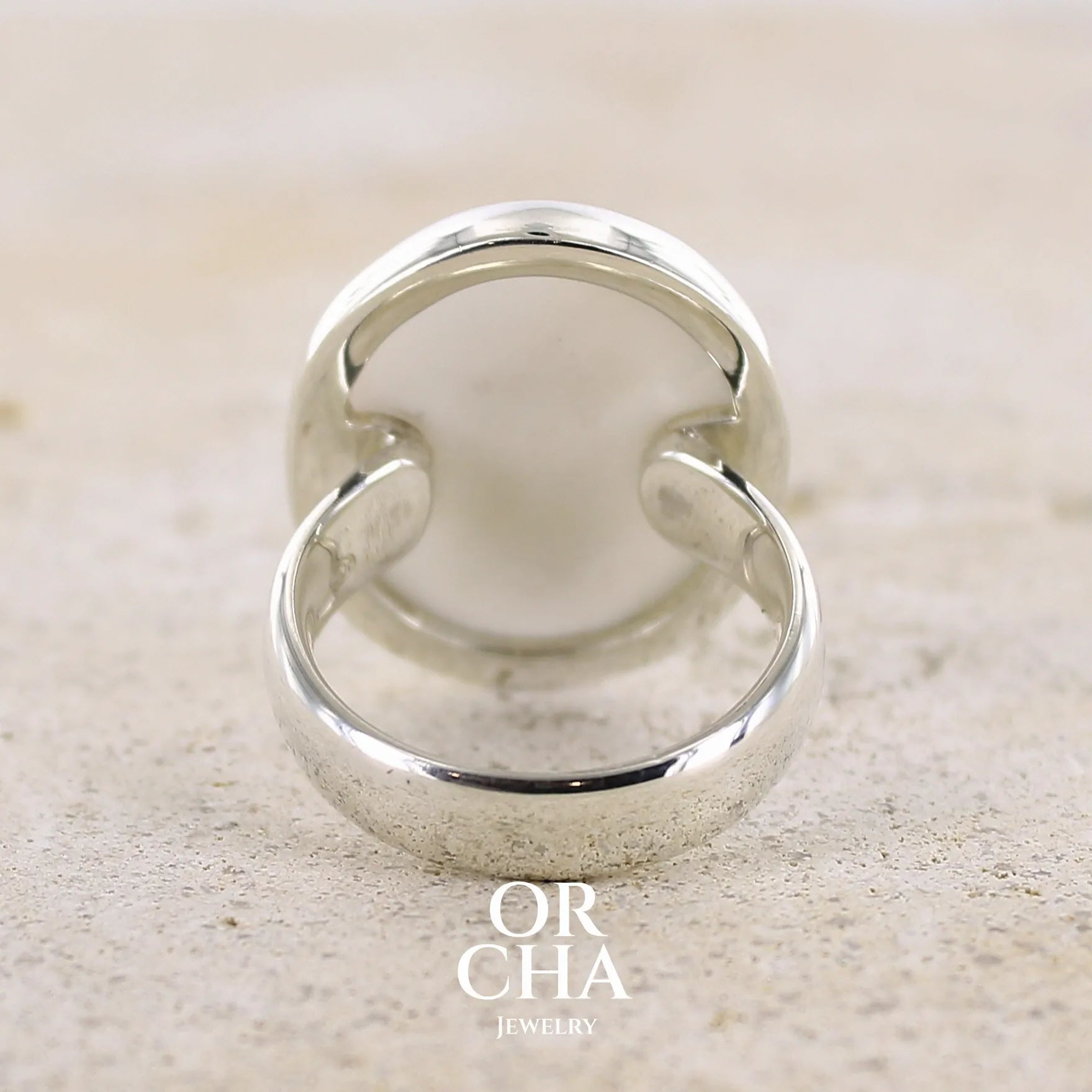 Vue de dos d'une bague pour femme en argent massif sertie d'un cabochon ovale d'agate dendritique de couleur blanc pur. Pierre opaque translucide à inclusions de dendrites de manganèse noires contrastées. Bijou unique réalisée en taille 56,5 par Orchajewelry