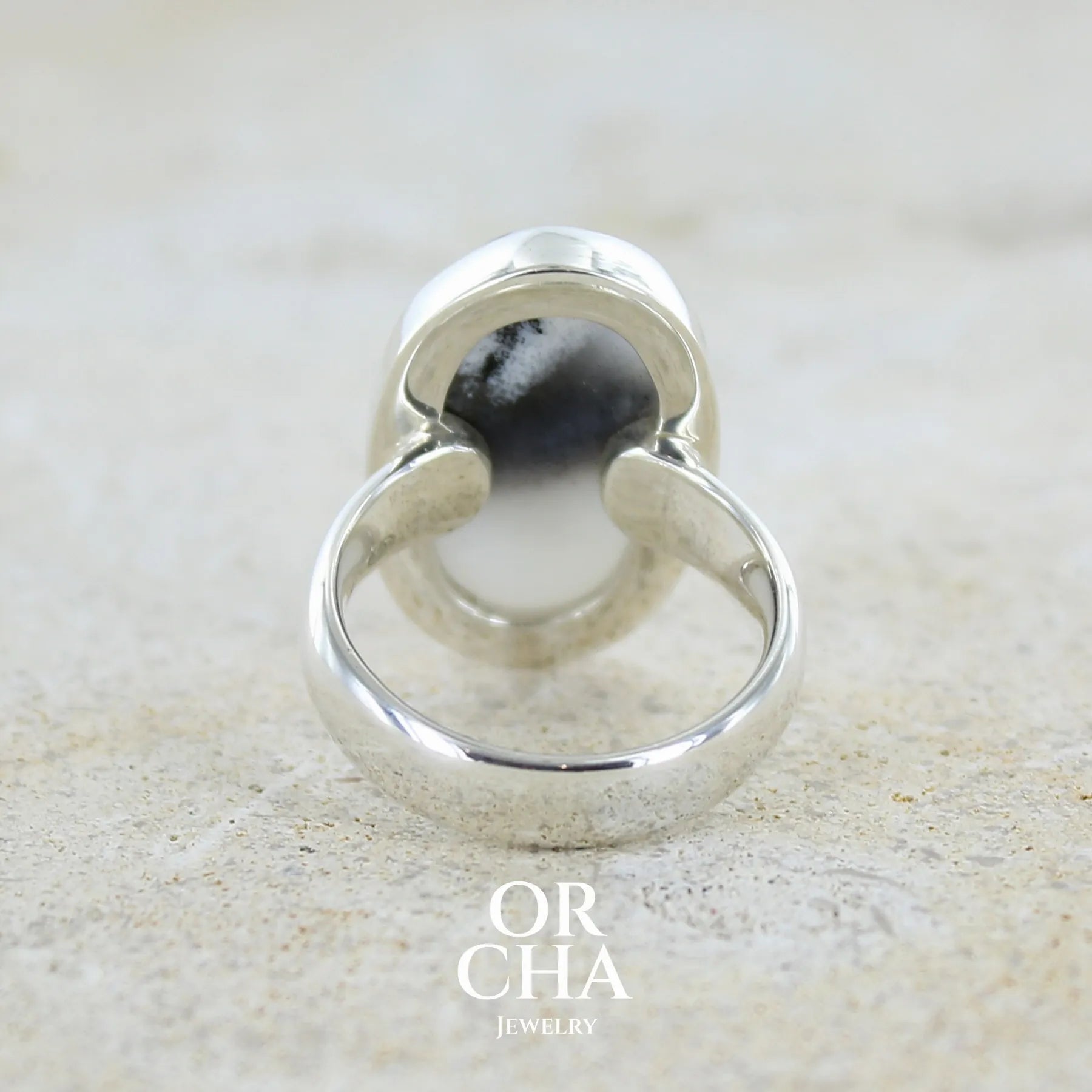 Vue de dos d'une bague pour femme en argent massif sertie d'un cabochon ovale d'agate dendritique de couleur blanc pur et noir. Pierre opaque translucide à inclusions paysages de dendrites de manganèse noires contrastées. Bijou unique réalisée en taille 54 par Orchajewelry