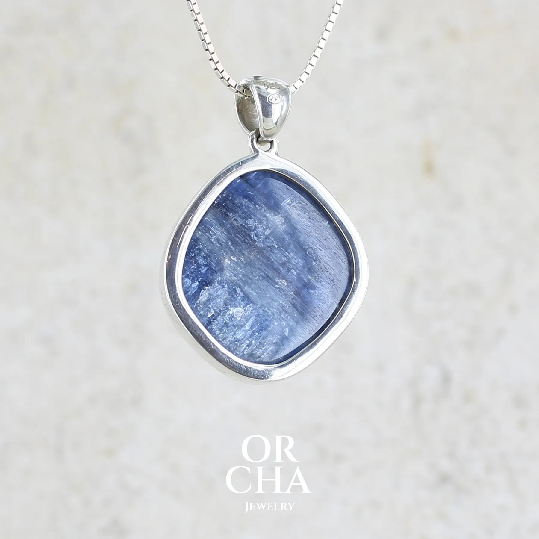 Vue de dos d'un pendentif en argent massif serti d'un cabochon de cyanite de couleur bleue jeans nacré. Pierre de qualité opaque comportant des inclusions. Bijoux unique par Orcha Jewelry