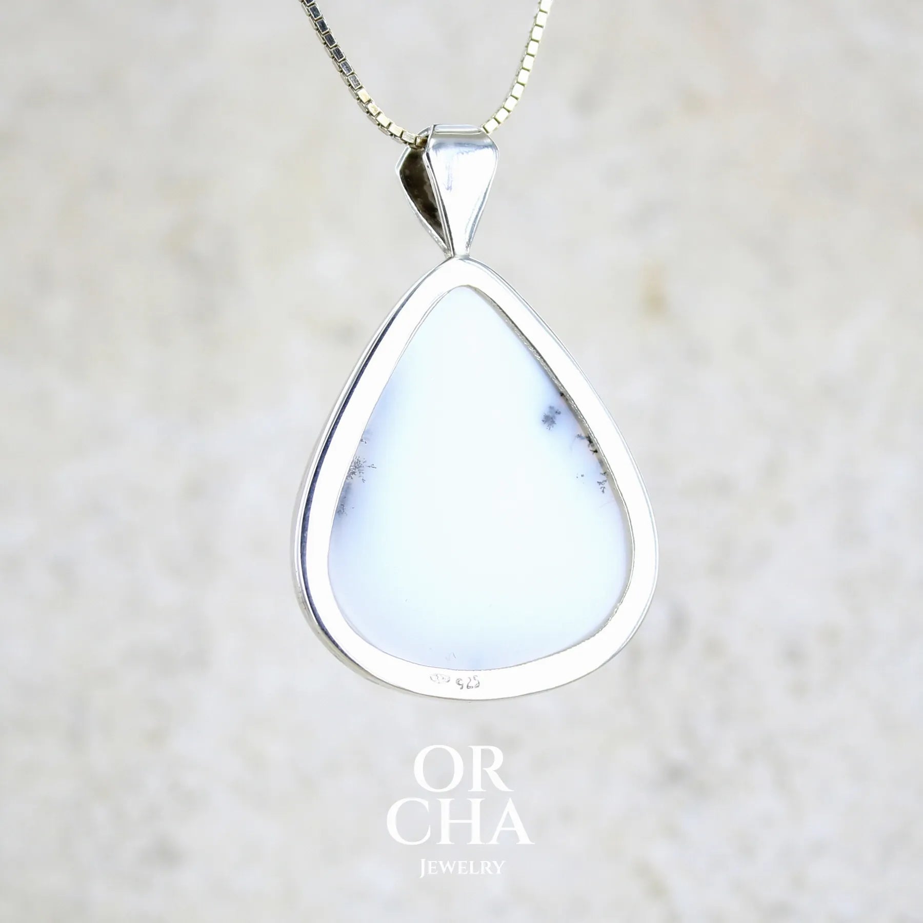 Vue de dos d'un pendentif pour femme en argent massif sertie d'un cabochon en forme de goutte d'agate dendritique de couleur blanc pur et noir. Pierre opaque à translucide à inclusions paysages de dendrites de manganèse noires contrastées. Bijou unique réalisé par Orchajewelry