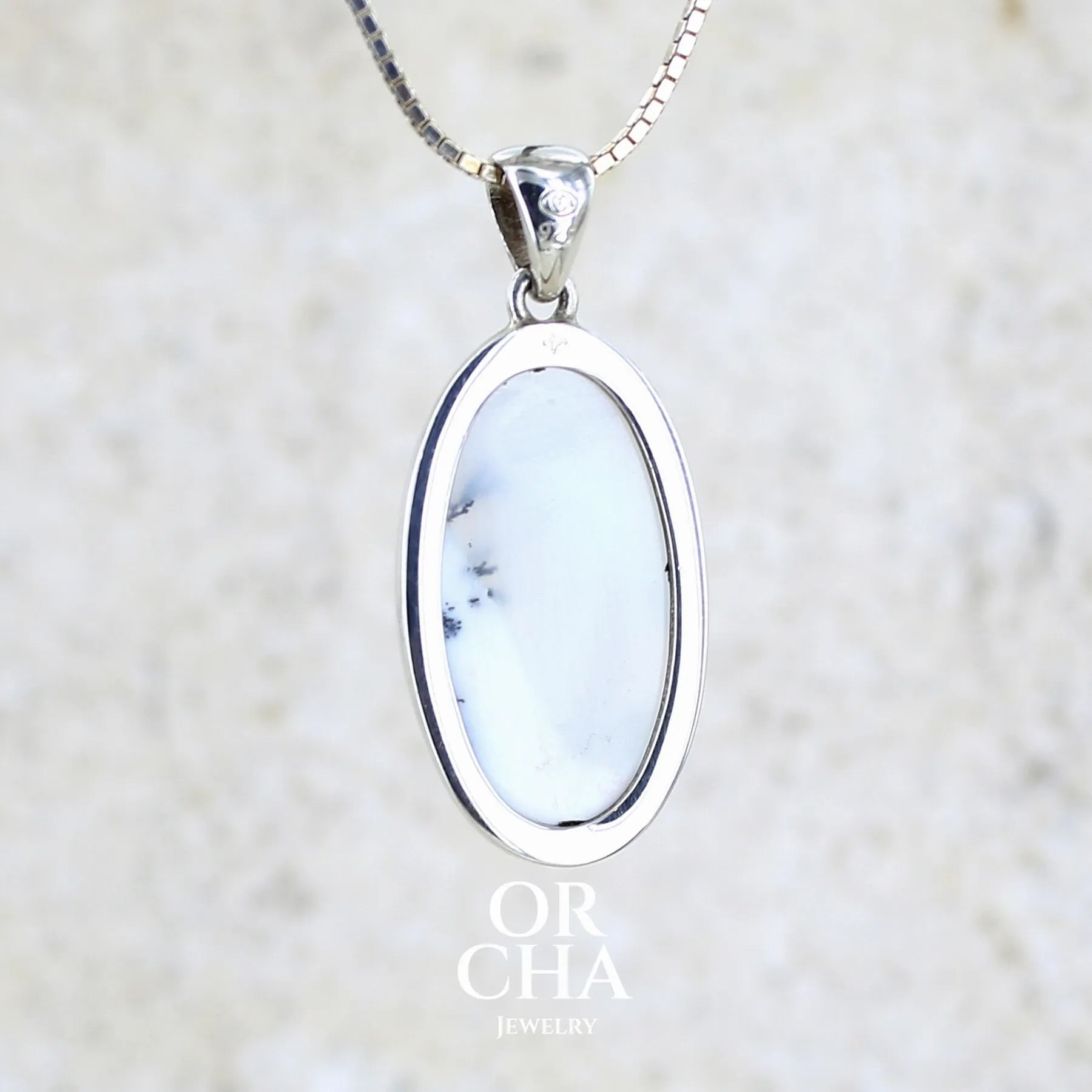 Vue de dos d'un pendentif pour femme en argent massif sertie d'un cabochon de forme ovale d'agate dendritique de couleur blanc pur et noir. Pierre opaque à translucide à inclusions paysages de dendrites de manganèse noires contrastées. Bijou unique réalisé par Orchajewelry